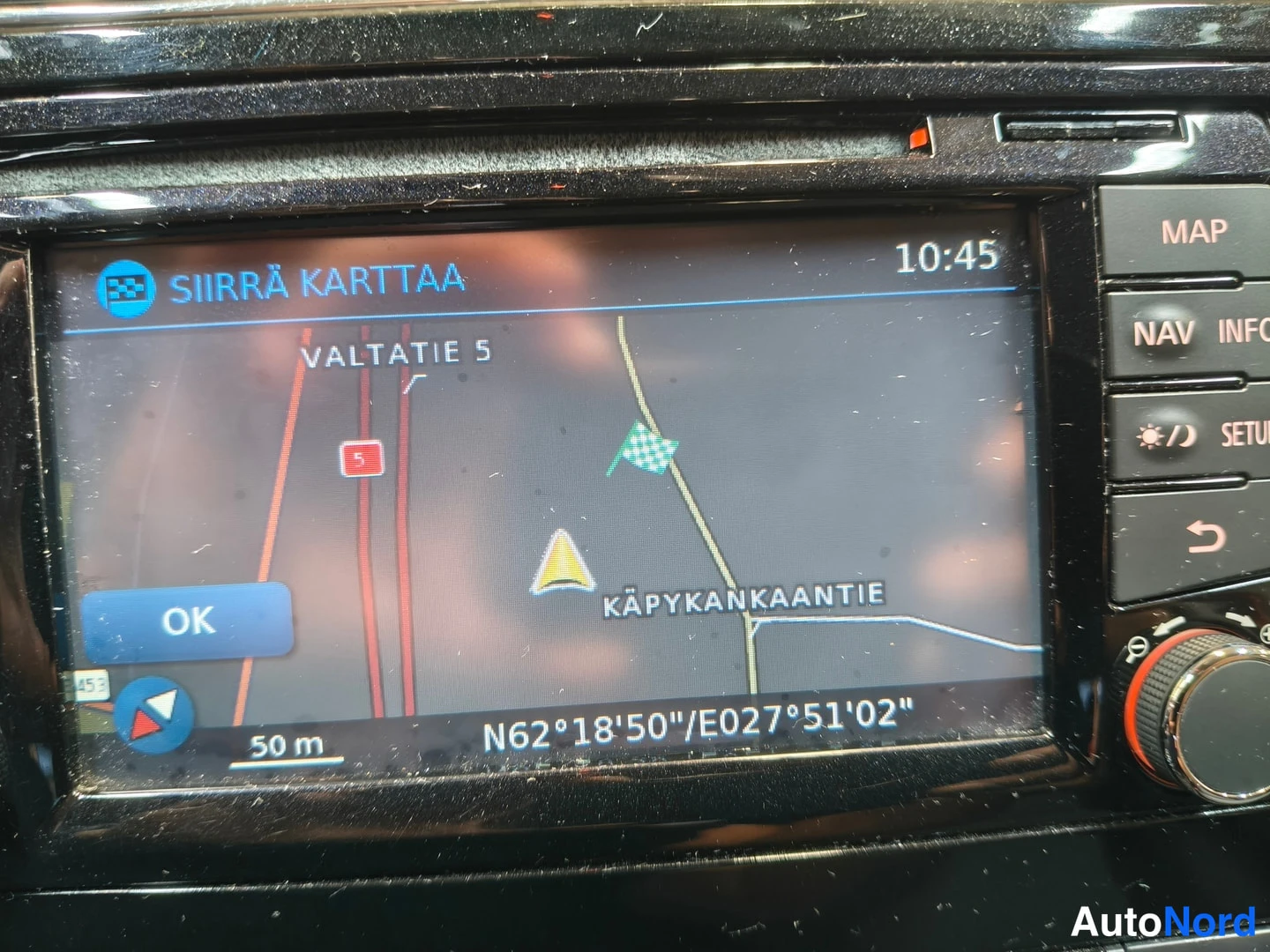 Muu: Navi- ja infotainment-näyttö, jossa kartta Valtatie 5 ja Käpykankaantie, koordinaatit N62°18'50/E027°51'02, kello 10:45.