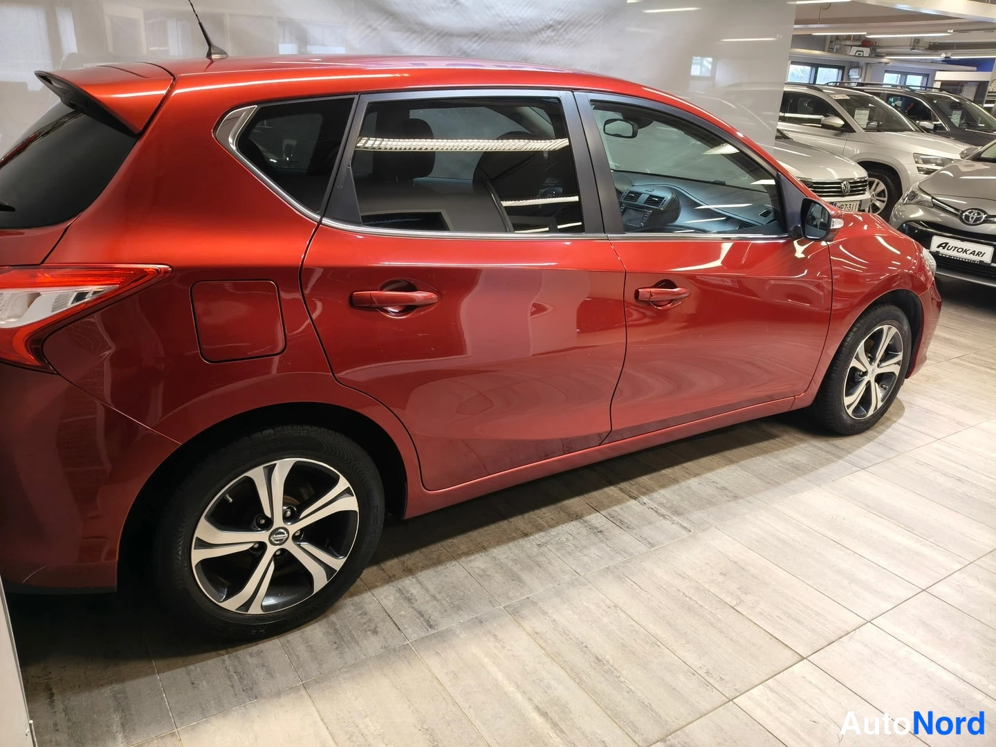 Sivulta: Punaisen Nissan Pulsar -henkilöauton kylki neljällä ovella ja viisikuumallisilla kevytmetallivanteilla autonhallissa.