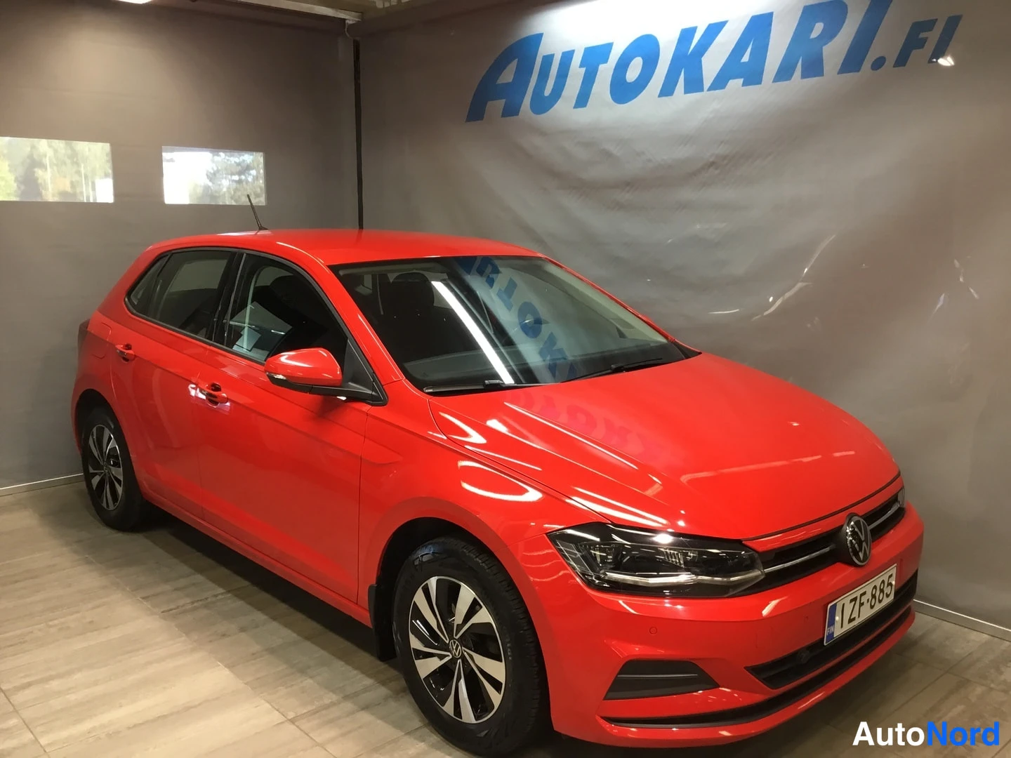 Etuviisto, nokka oikealle: Punainen Volkswagen Polo viistosti edestä oikealta kuvattuna autosalissa, rekisteritunnus ZF-885.