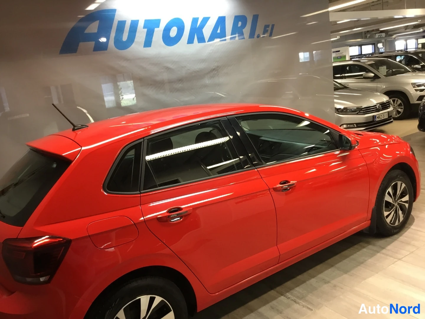 Takaviisto: Punainen Volkswagen Polo viistosti takaa vasemmalta kuvattuna autosalissa, taustalla muita autoja.