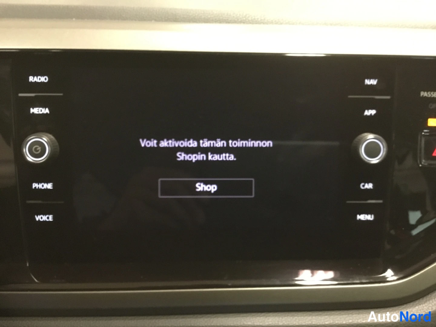 Yksityiskohta: Auton infotainment-näyttö, jossa lukee 'Voit aktivoida tämän toiminnon Shopin kautta.' ja Shop-painike; sivuilla RADIO, MEDIA, PHONE, VOICE, NAV, APP, CAR ja ME