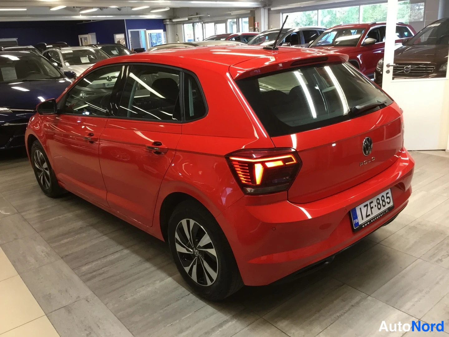 Takaviisto: Punainen Volkswagen Polo viistosti takaa vasemmalta kuvattuna autosalissa, rekisteritunnus ZF-885.