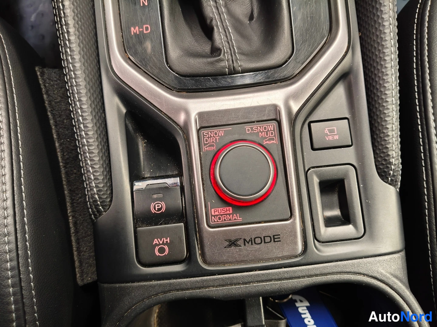 Yksityiskohta: Keskikonsolin Hallintanapit: X-MODE-painike, jossa tekstit SNOW, DIRT, D.SNOW, MUD ja PUSH NORMAL, sekä elektronisen parkkijarrun (P) ja AVH-painike.
