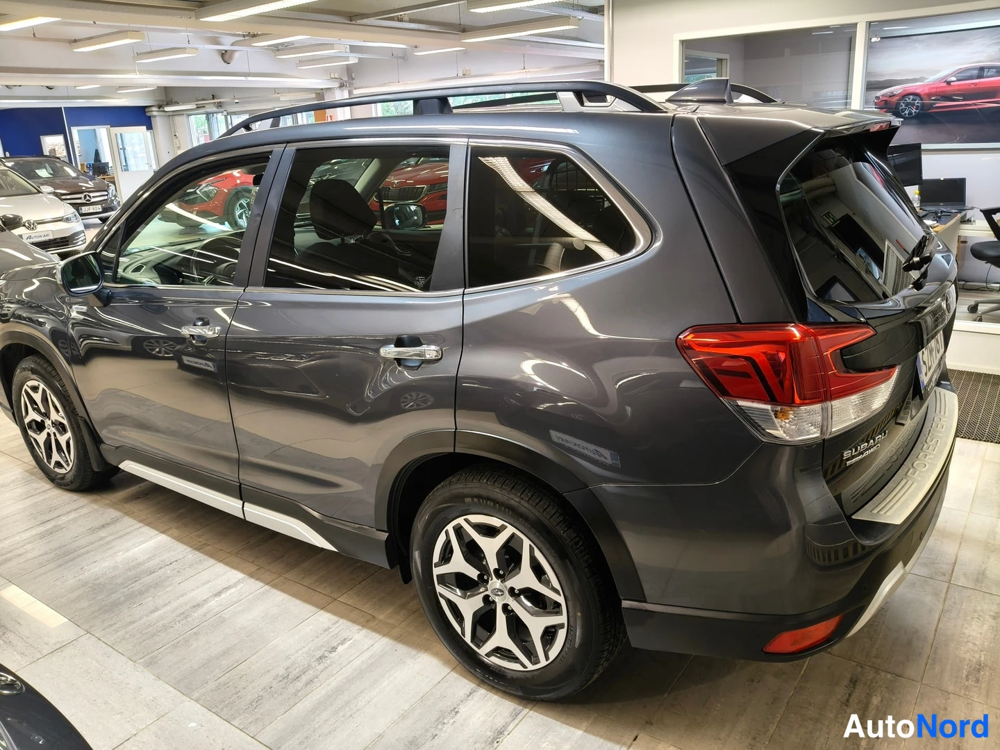 Takaviisto: Tummanharmaa Subaru Forester tak kolmasosasta vasemmalta, perä ja kylki näkyvät sisätiloissa.