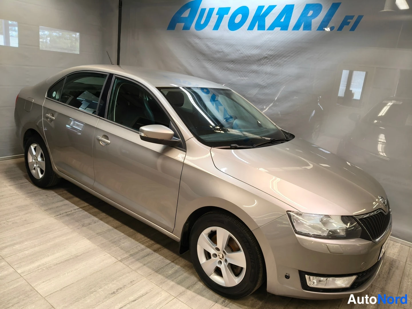 Etuviisto, nokka oikealle: Škoda Rapid -sedan etuviistosta oikealta kuvattuna sisätiloissa, vaaleanbeige kori ja hopeanvalkoiset vanteet.