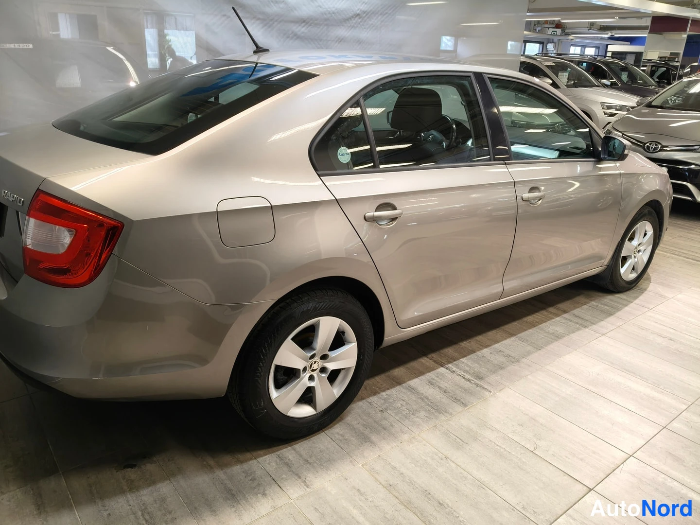 Takaviisto: Hopeanharmaa Škoda Rapid sedan vasemmalta taakse kuvattuna, takavalo ja RAPID-teksti näkyvät