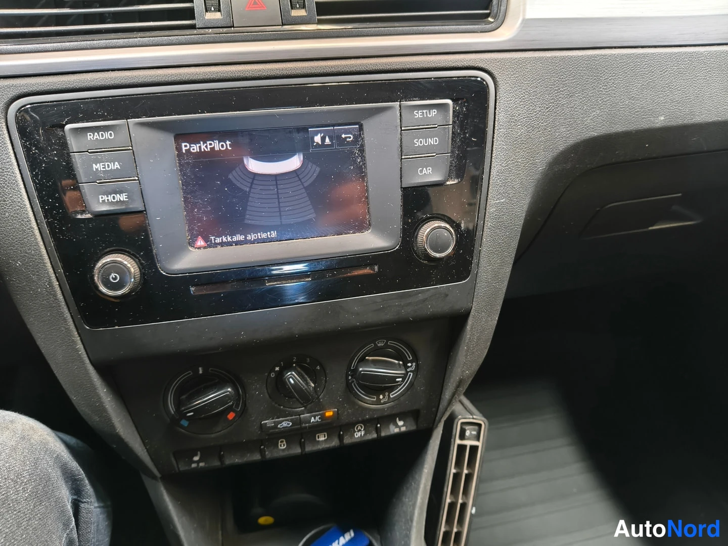 Yksityiskohta: Keskeinen näyttö, jossa lukee 'ParkPilot' ja tekstim粉 'Tarkalle ajotietä!', ympärillä RADIO-, MEDIA-, PHONE-, SETUP-, SOUND- ja CAR-painikkeet.