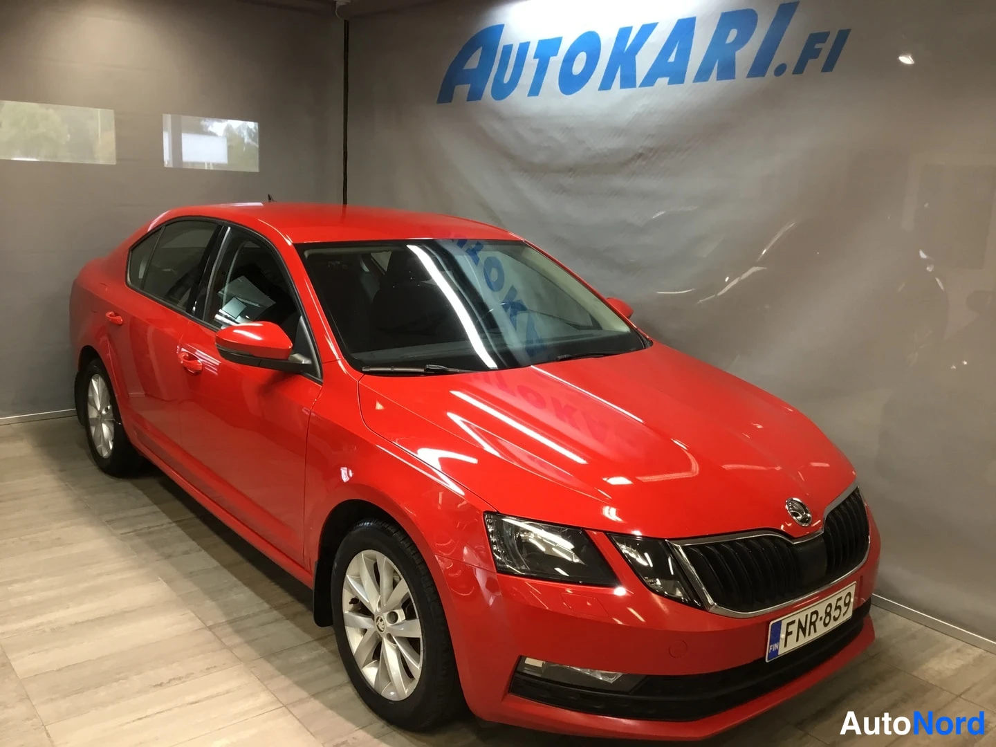 Etuviisto, nokka oikealle: Punainen sedan etuosa kolmivartalokuvassa, rekisterikilpi, sisätiloissa Autokari.fi-taustaa vasten.