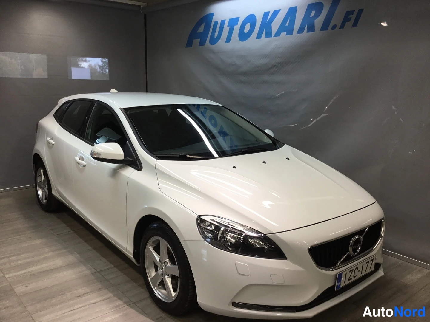 Etuviisto, nokka oikealle: White Volvo hatchback photographed indoors at a front three-quarter angle, nose pointing right.