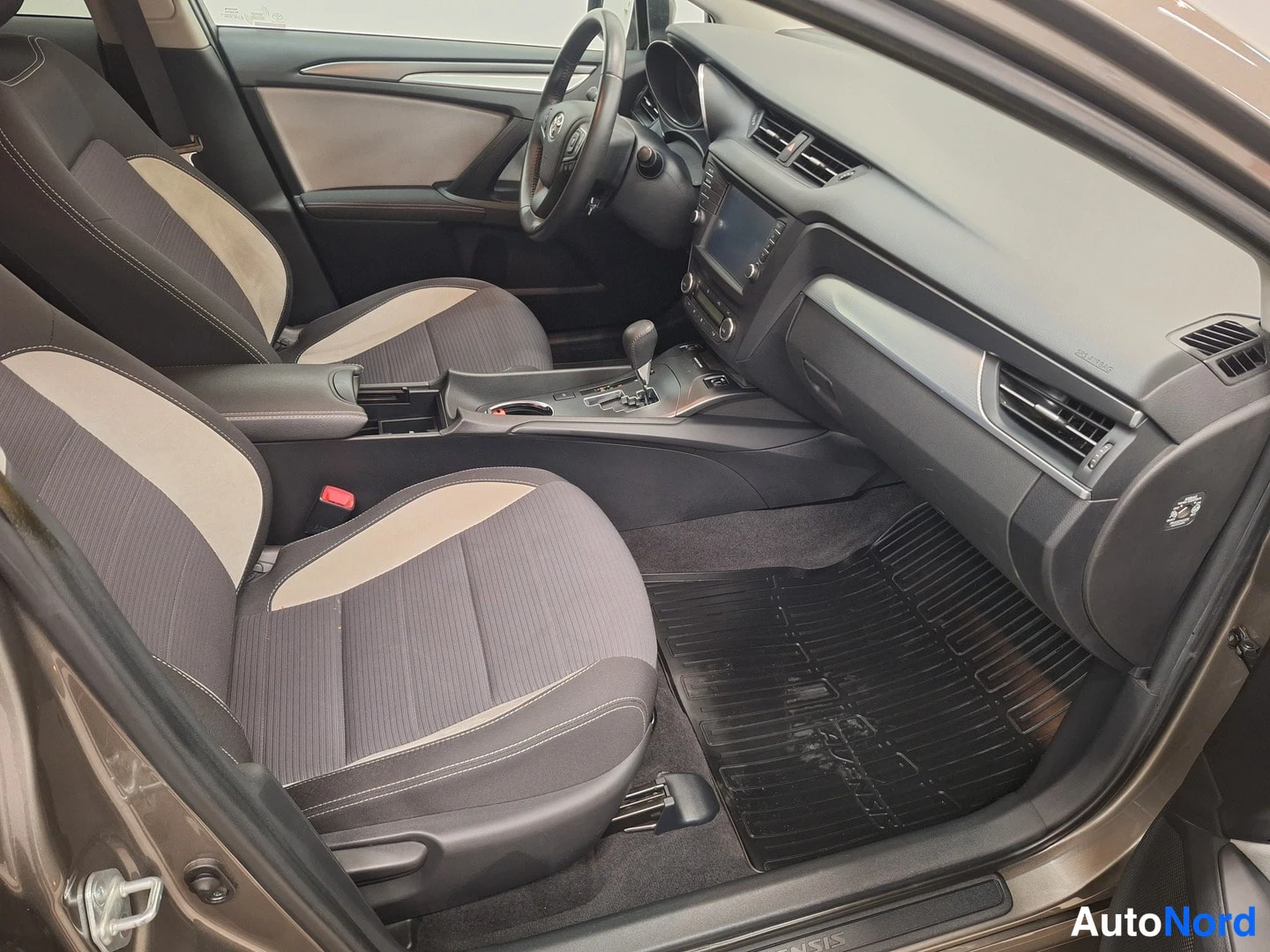 Edestä: Etumatkustajan puoleinen sisätilanäkymä: harmaa-beige penkit, automaattivaihteen valitsin, infotainment-näyttö ja kumimatot.