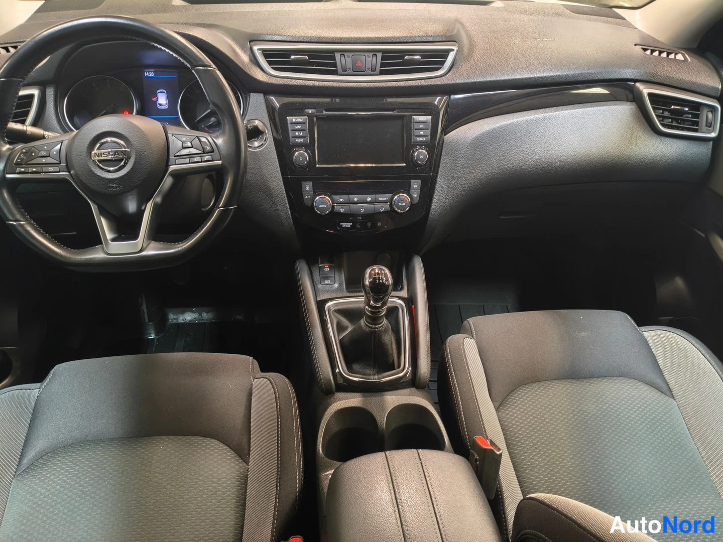 Edestä: Auton sisätila etusiltä: Nissan-ohjauspyörä, kojelauta, vaijeri ja tummat kankaanistuimet.