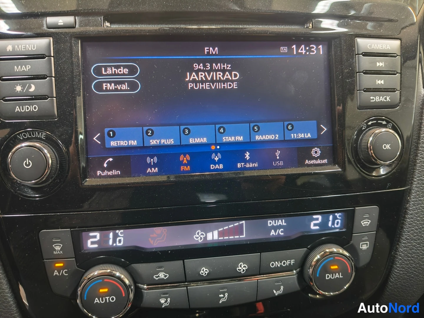 Edestä: Radio näyttää FM-taajuuden 94,3 MHz JARVIRAD Puheluviide, esiasetukset ja lähteet kuten DAB ja USB, alla 21 asteen ilmastointi.