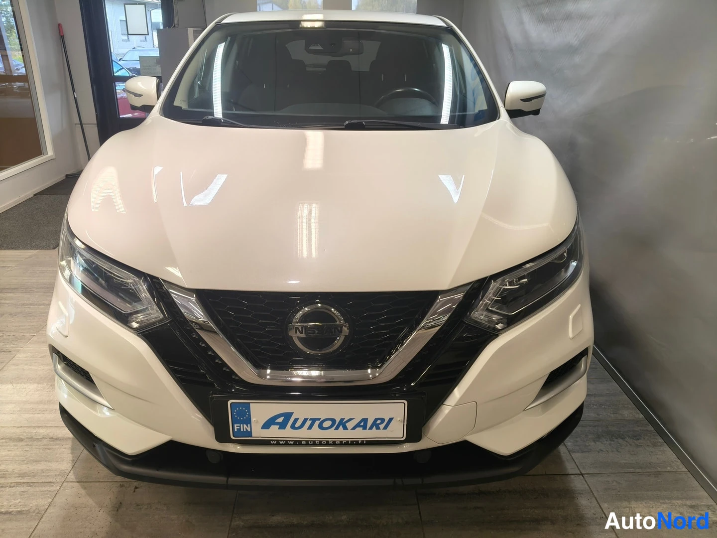 Edestä: Nissan Qashqai suoraan edestä valkoinen, Nissan-merkki konepellin alla, Autokari-kilpi rekisterikilven paikalla.
