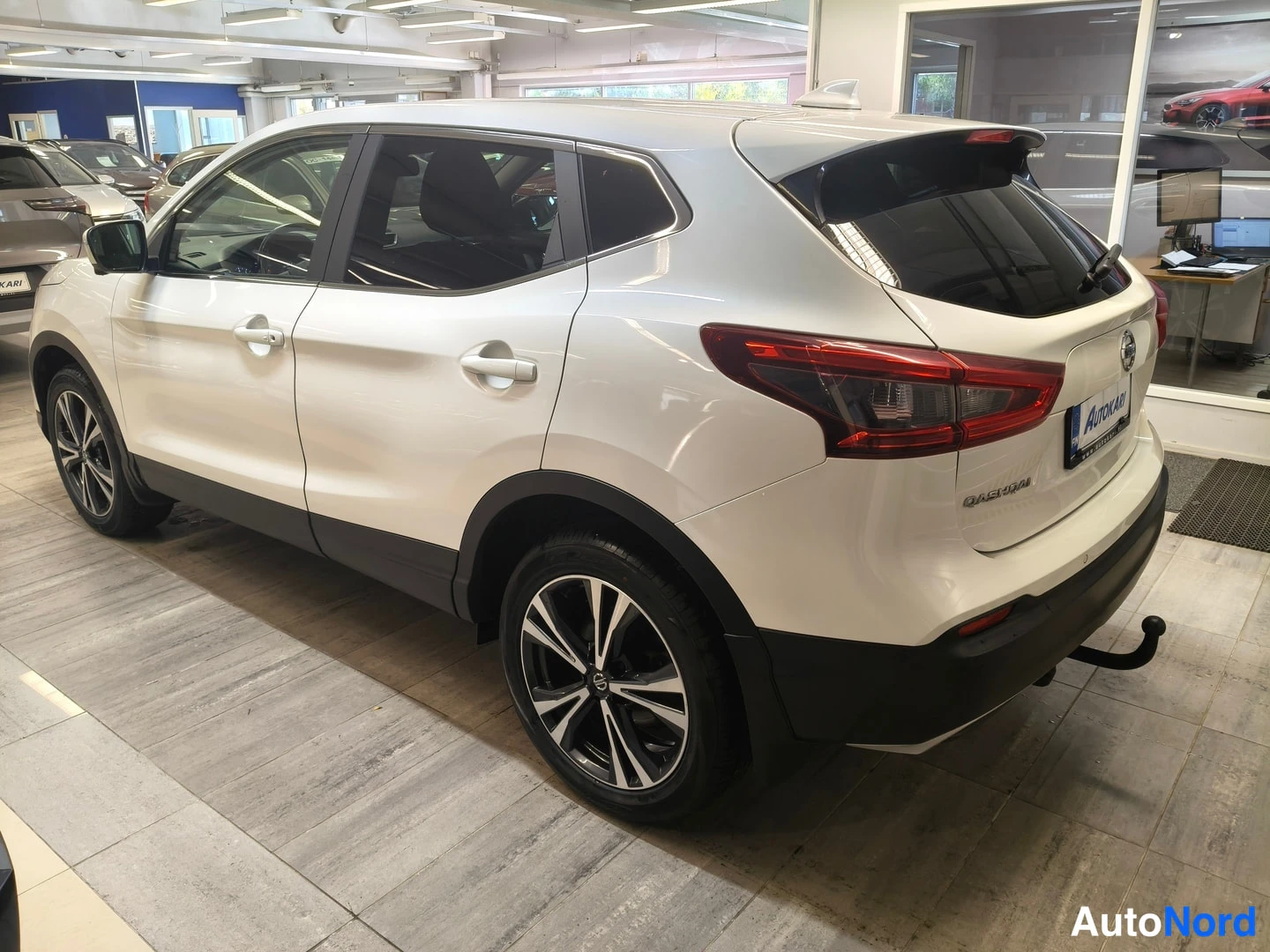 Takaviisto: Nissan Qashqai valkoinen takaviisto kuvattu oikealta showroomissa, perävaunu-kytkin, kattoluistimet ja Qashqai-tunnus näkyvät.