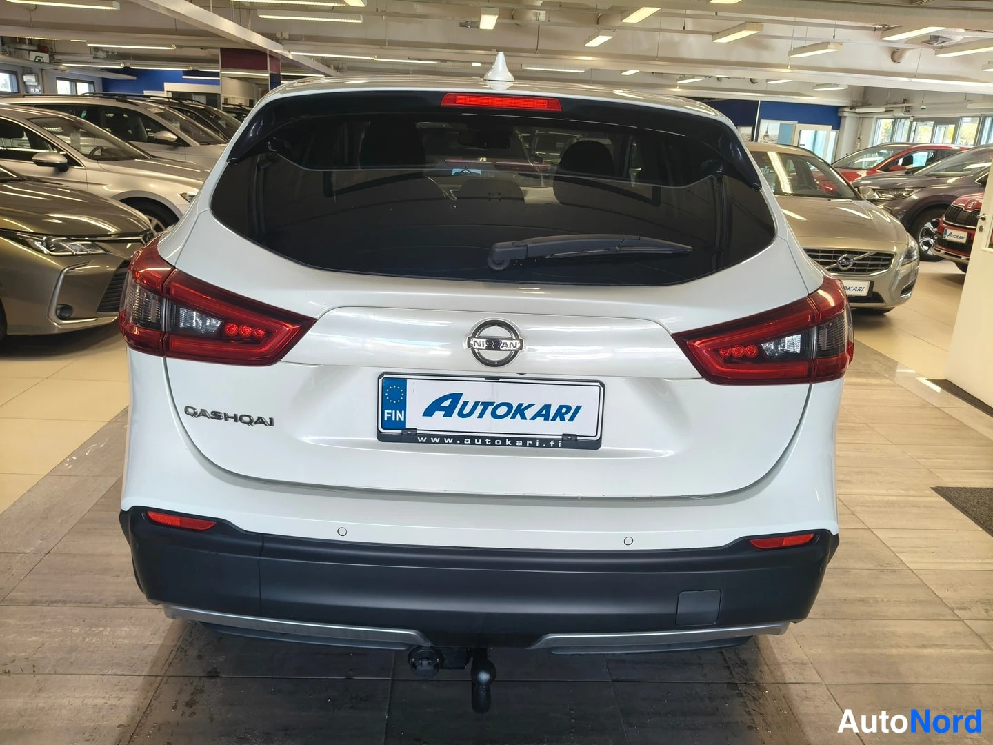 Takaa: Auton takanäkymä: valkoinen Nissan Qashqai, punaiset takavalot, Nissan-merkki ja Qashqai-teksti, Autokari-rekisterikilven suojakehys sekä veto koukku takapuskas
