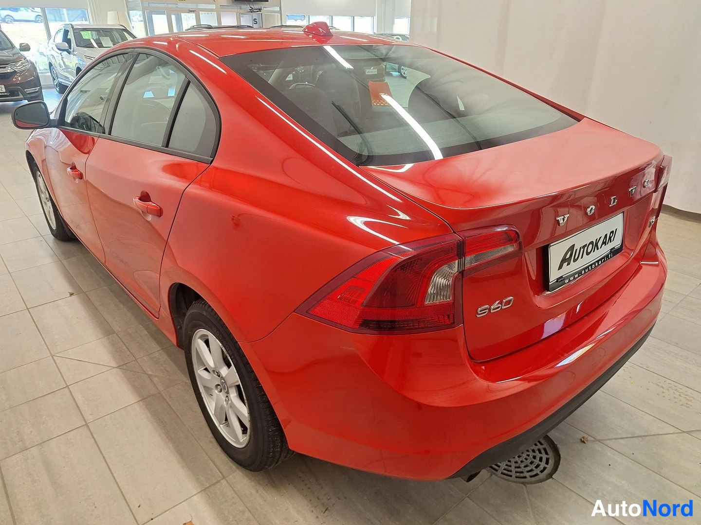 Takaviisto: Volvo S60 -sedanin takakulma autonhallissa: punainen kori, takavalot ja Autokari-kyltti näkyvät.