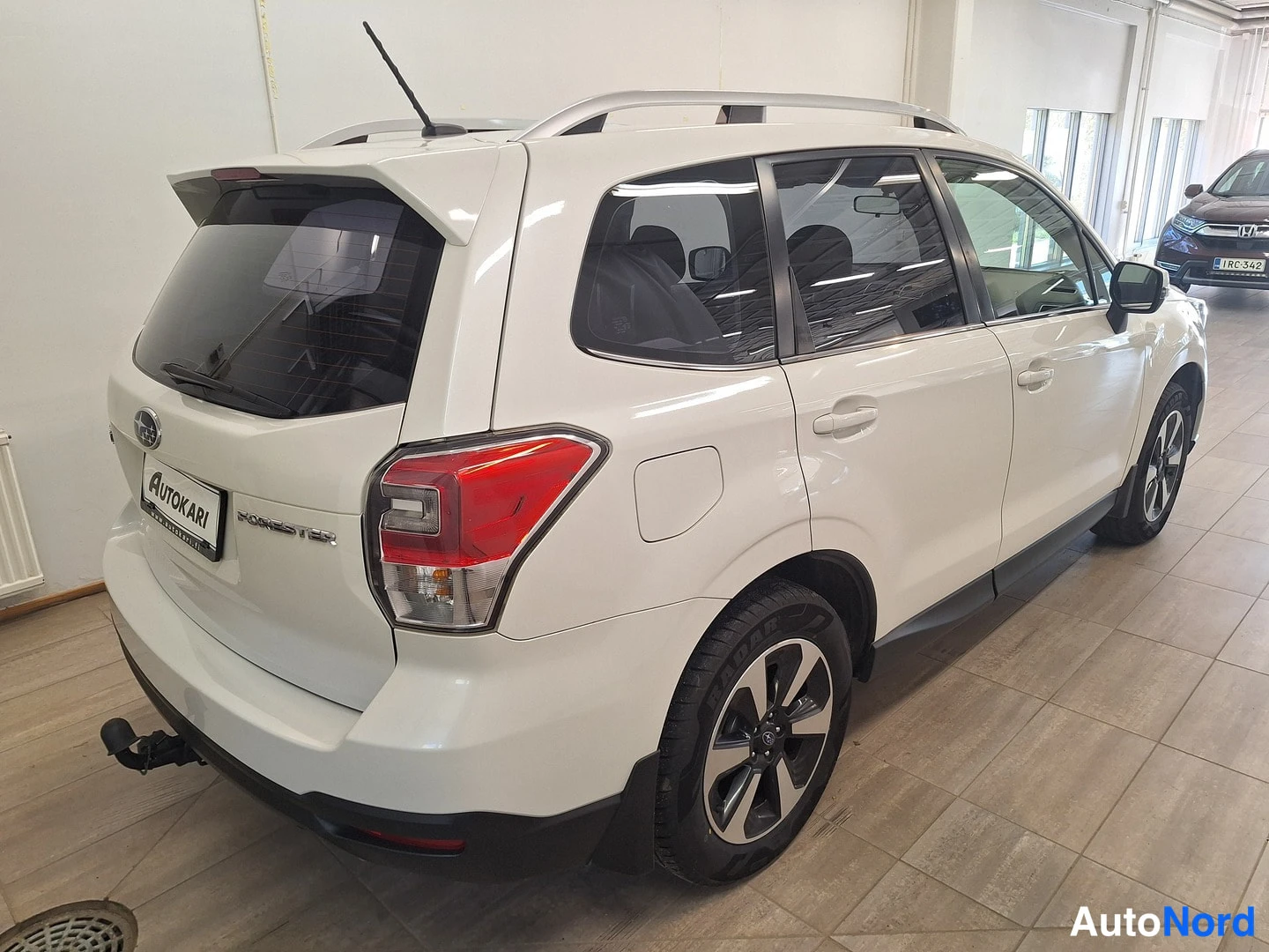 Takaviisto: Valkoinen Subaru Forester takaviistosta oikealta, takapaneeli ja kyljen ovet näkyvissä sisätiloissa.