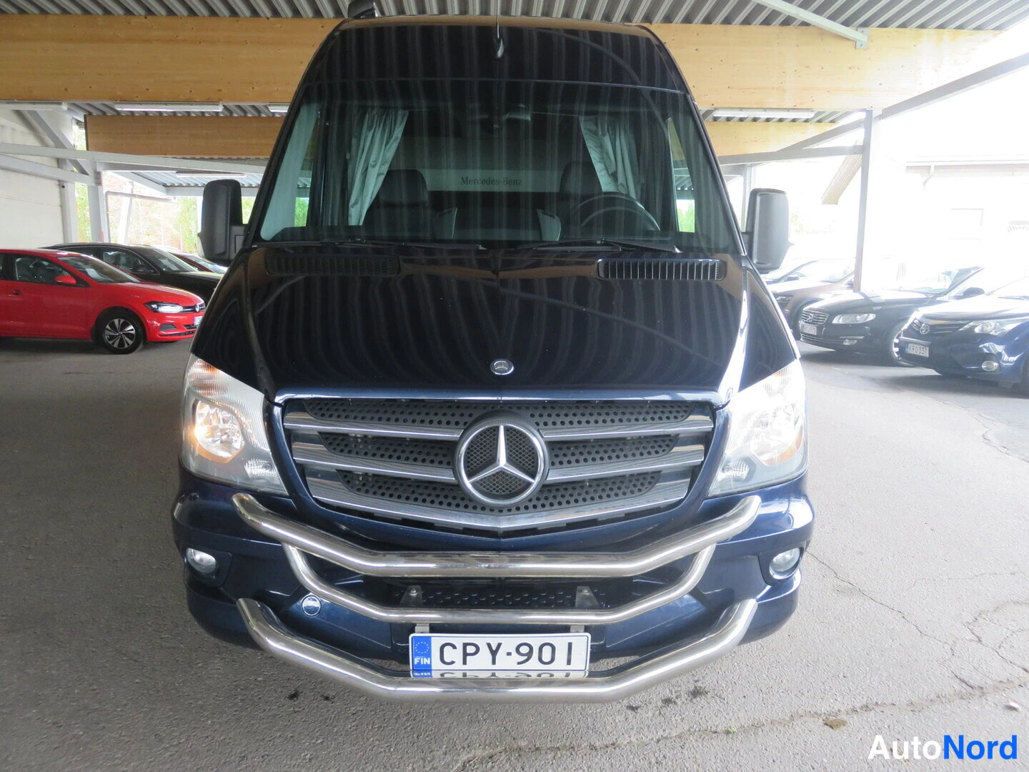 Edestä: Mercedes-Benz Sprinter -pakettiauto suoraan edestä kuvattuna, konepellillä tunnus ja etupuskurissa kromiläyttö, rekisterikilpi.