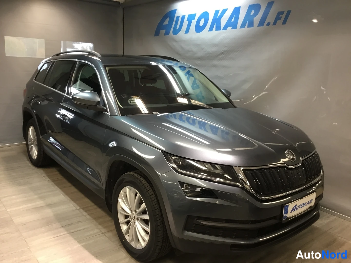 Etuviisto, nokka oikealle: Karmahtavanharmaa Skoda Kodiaq etuviistosta oikealta sisätiloissa, keulapuskuri ja kylki näkyvät.