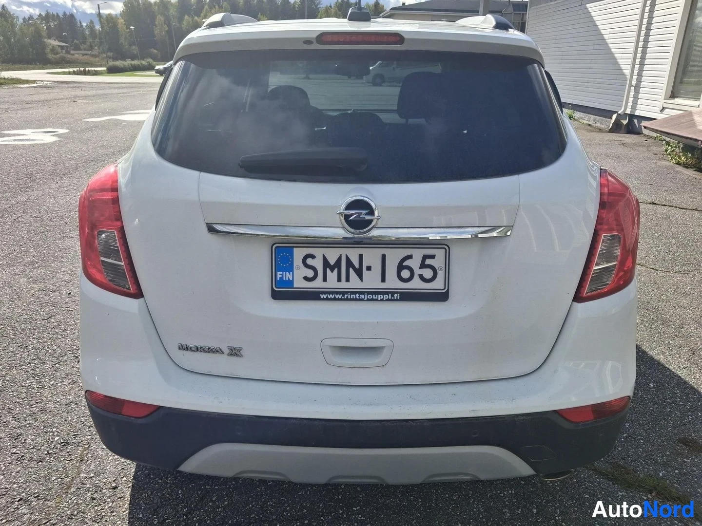 Takaa: Takakuvassa näkyy valkoinen Opel Mokka X -auto pysäköitynä asfaltilla. Autossa on Finnish-lisenssimerkki.