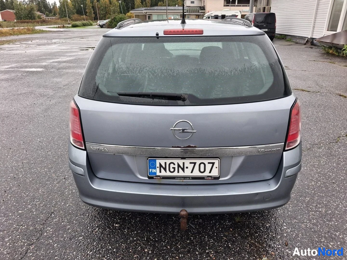 Takaa: Opel Astra Farmarin perä takaa nähtynä; rekisteritunnus, sininen EU-tunnus, Opel-embleemi ja ASTRA-teksti kannessa, vetokoukku.