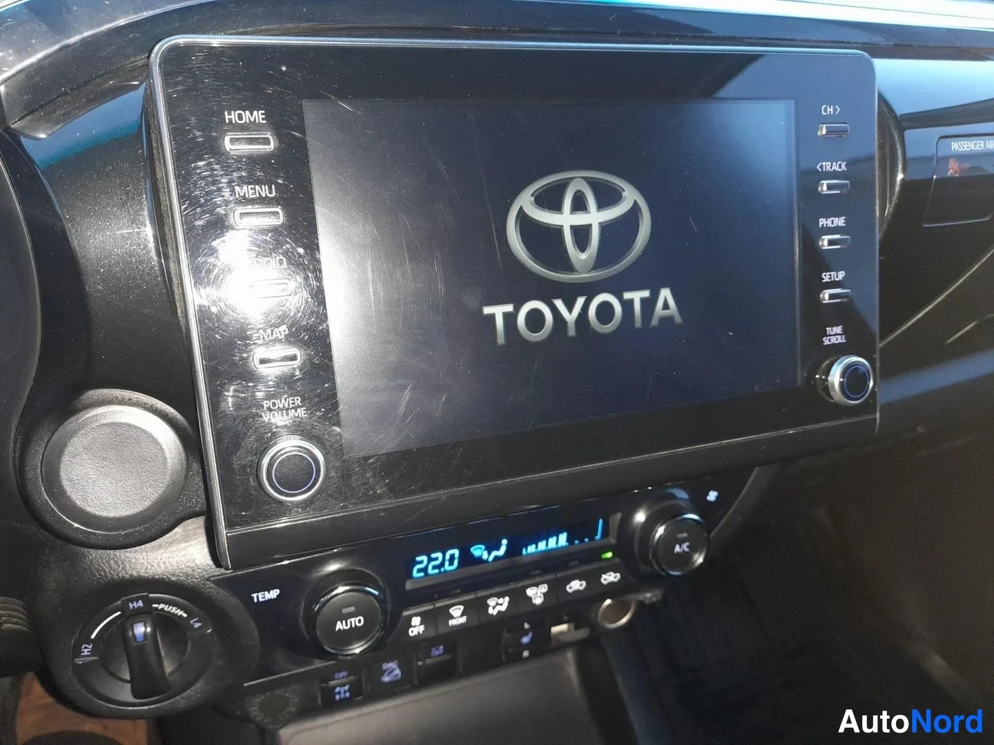Muu: Kojelaudan keskikonsoli Toyota-merkinnällä: kosketusnäyttö, automaattinen ilmastointi (AUTO), lukema 22,0 astetta ja A/C-nappi.