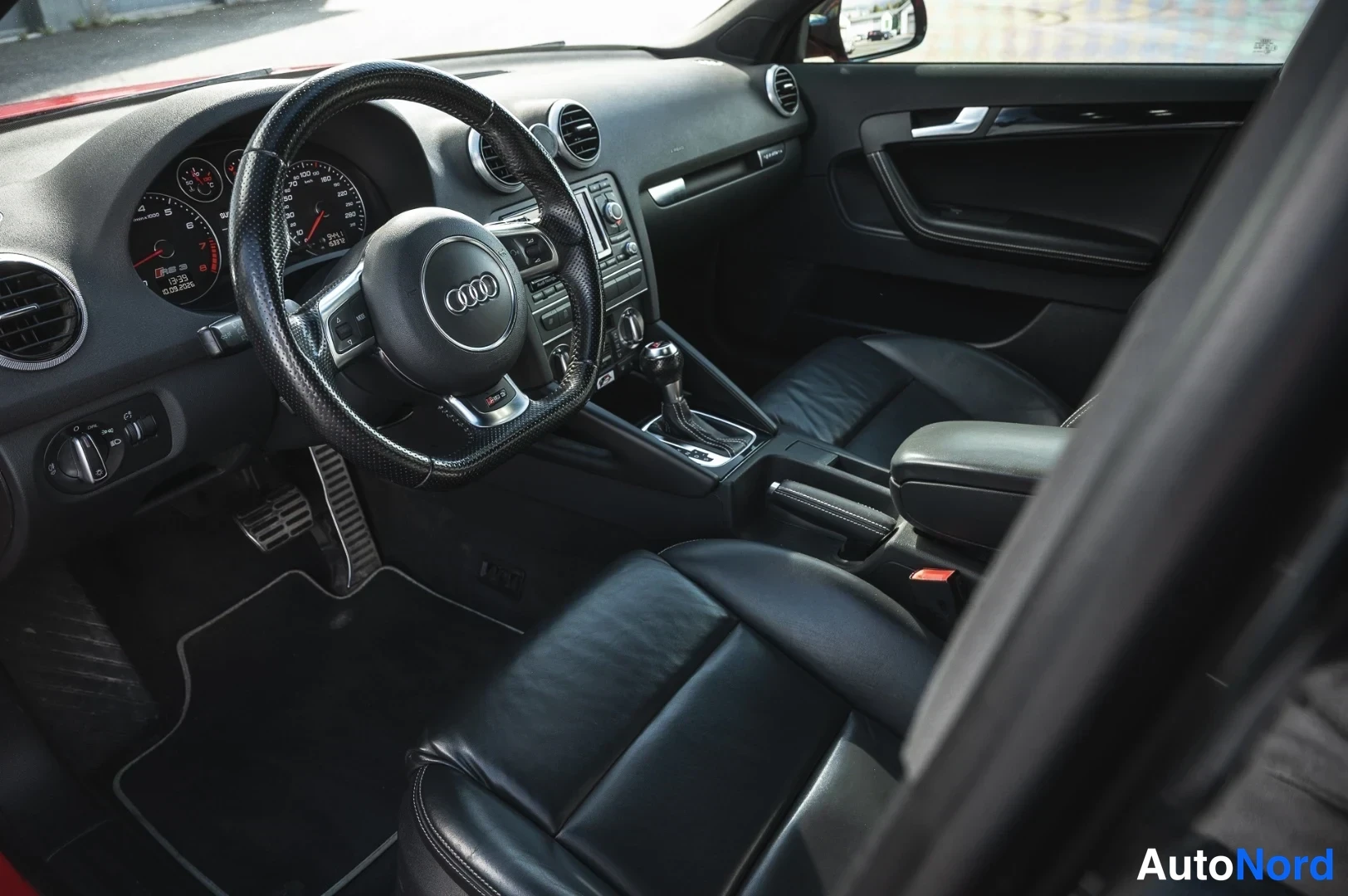 Muu: Ohjaamo vasemmalta: Audi-ratti, analogiset mittarit, automaattivaihtopyörä ja mustat nahkaistuimet.