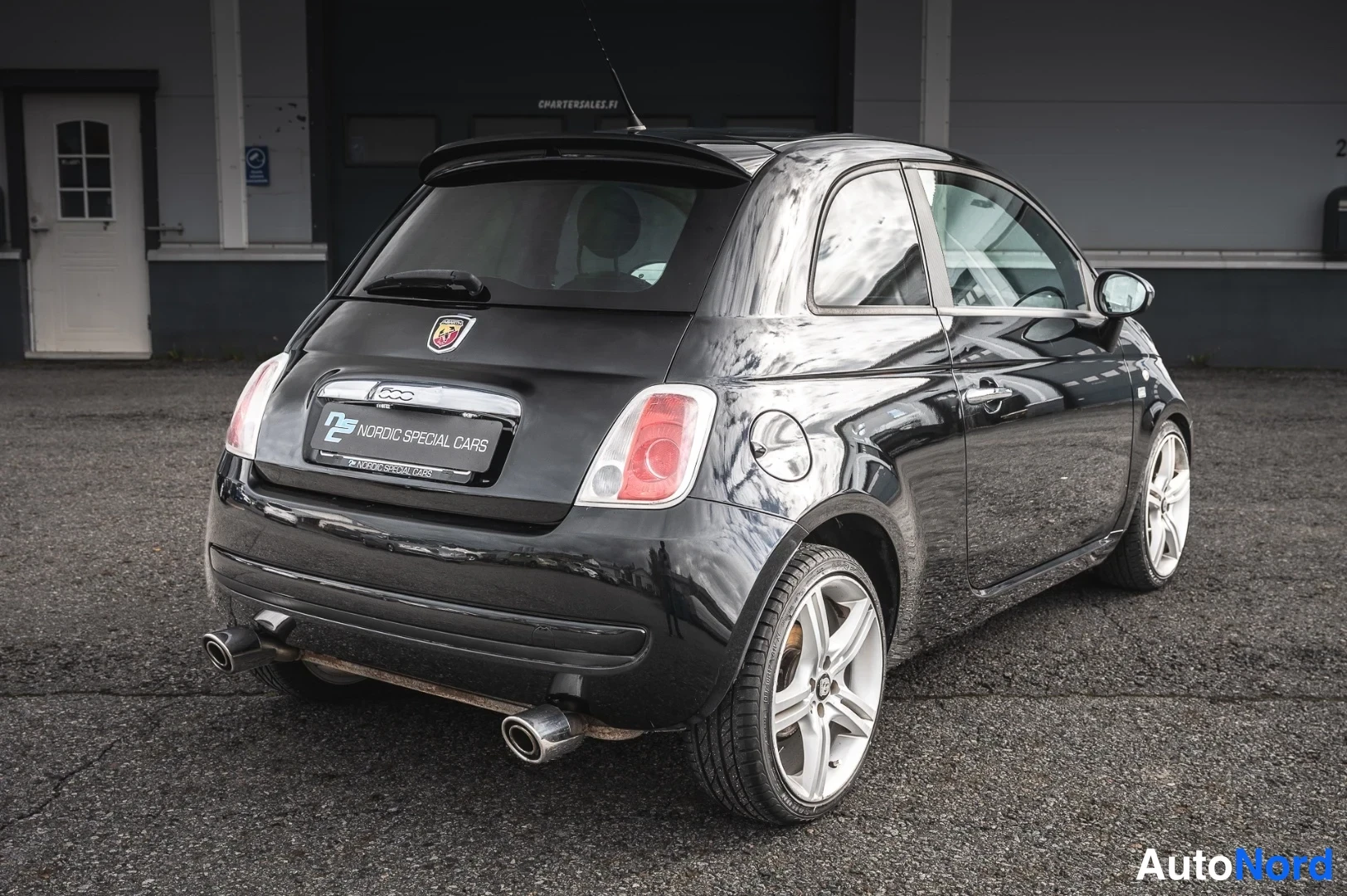 Takaviisto: Mustan Fiat 500:n takakulmakuva, kaksiosainen pakoputki ja hopeiset vanteet näkyvissä.