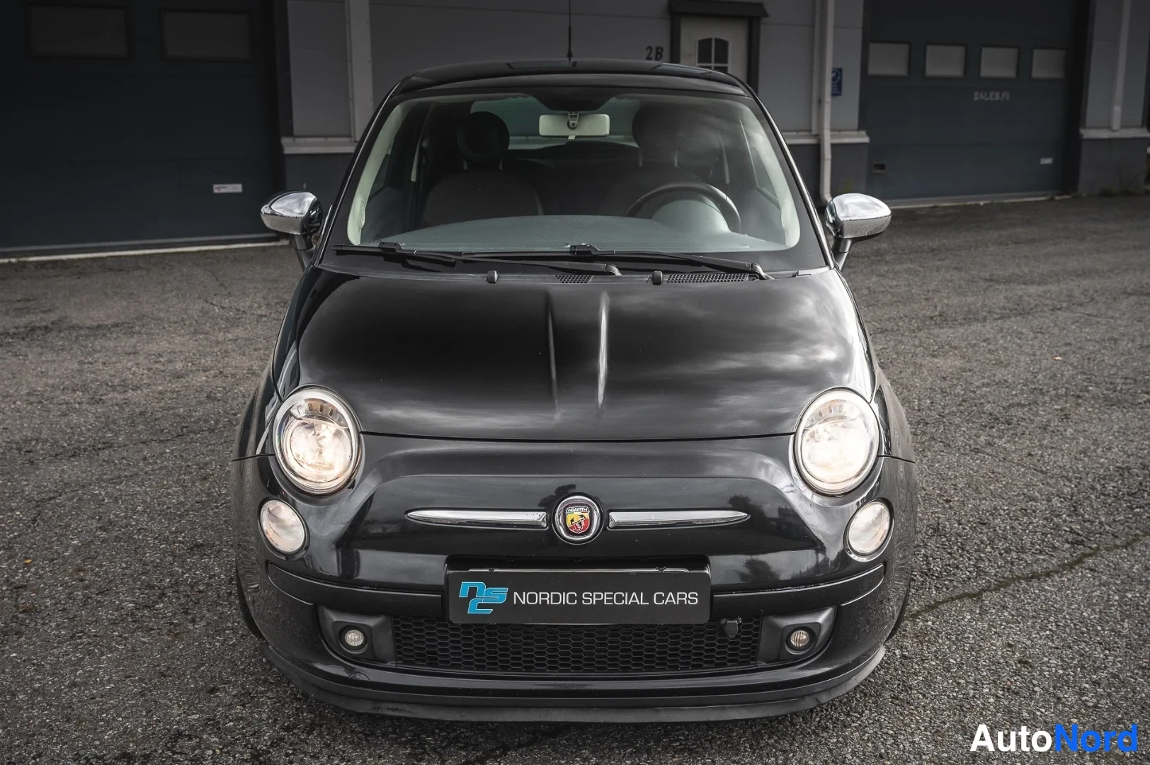 Edestä: Mustan Fiat 500:n suora etukuva, pyöreät ajovalot ja korimerkki näkyvissä.