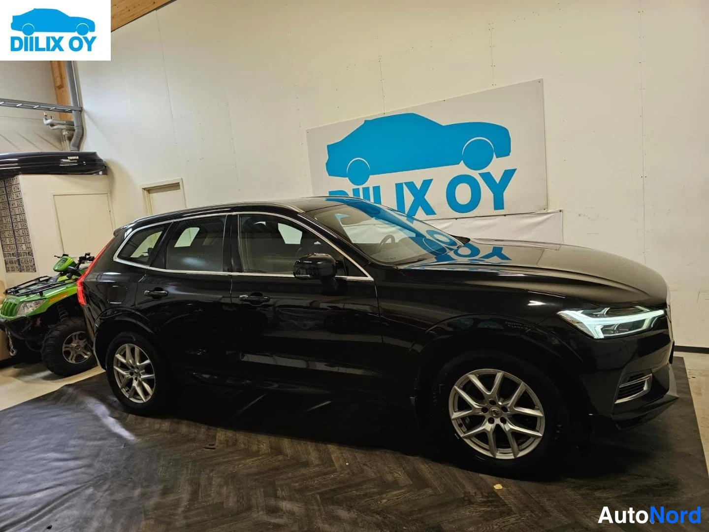 Sivulta: Mustan Volvo XC60:n sivukulma sisätiloissa, etusarvi ja etupyörä näkyvät oikealla.