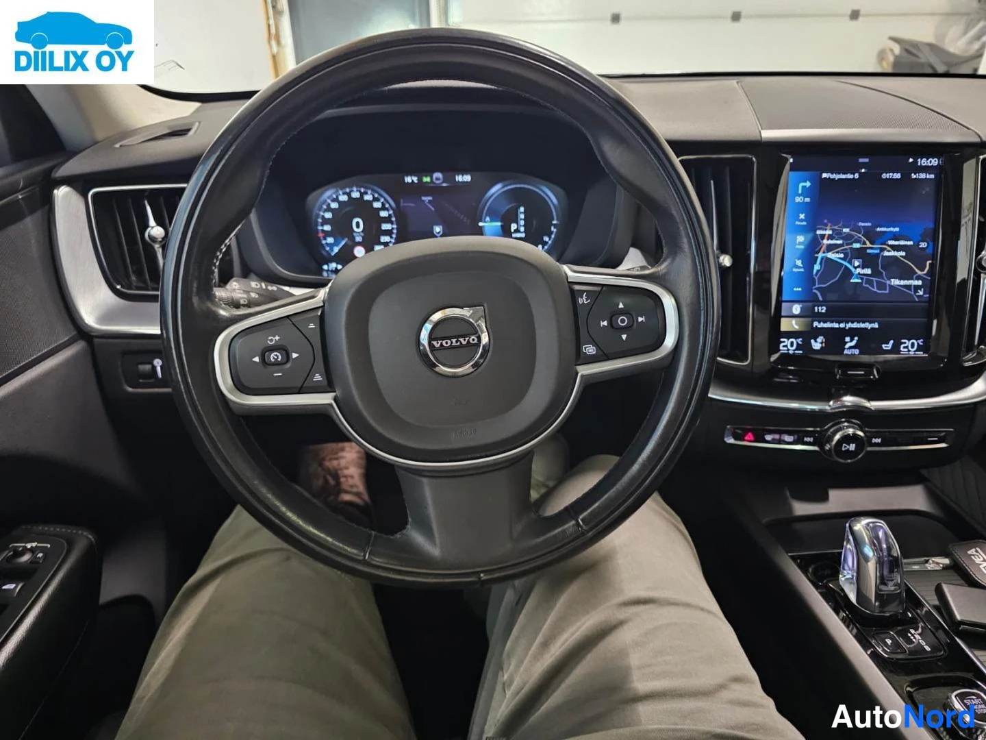 Muu: Ohjaamo keltaisen Volvo-stiiran taakse kuvattuna: Volvo-merkitty ohjauspyörä, digitaalinen mittaristo ja keskikonsolin infotainment-näyttö, jossa näkyy kartta.