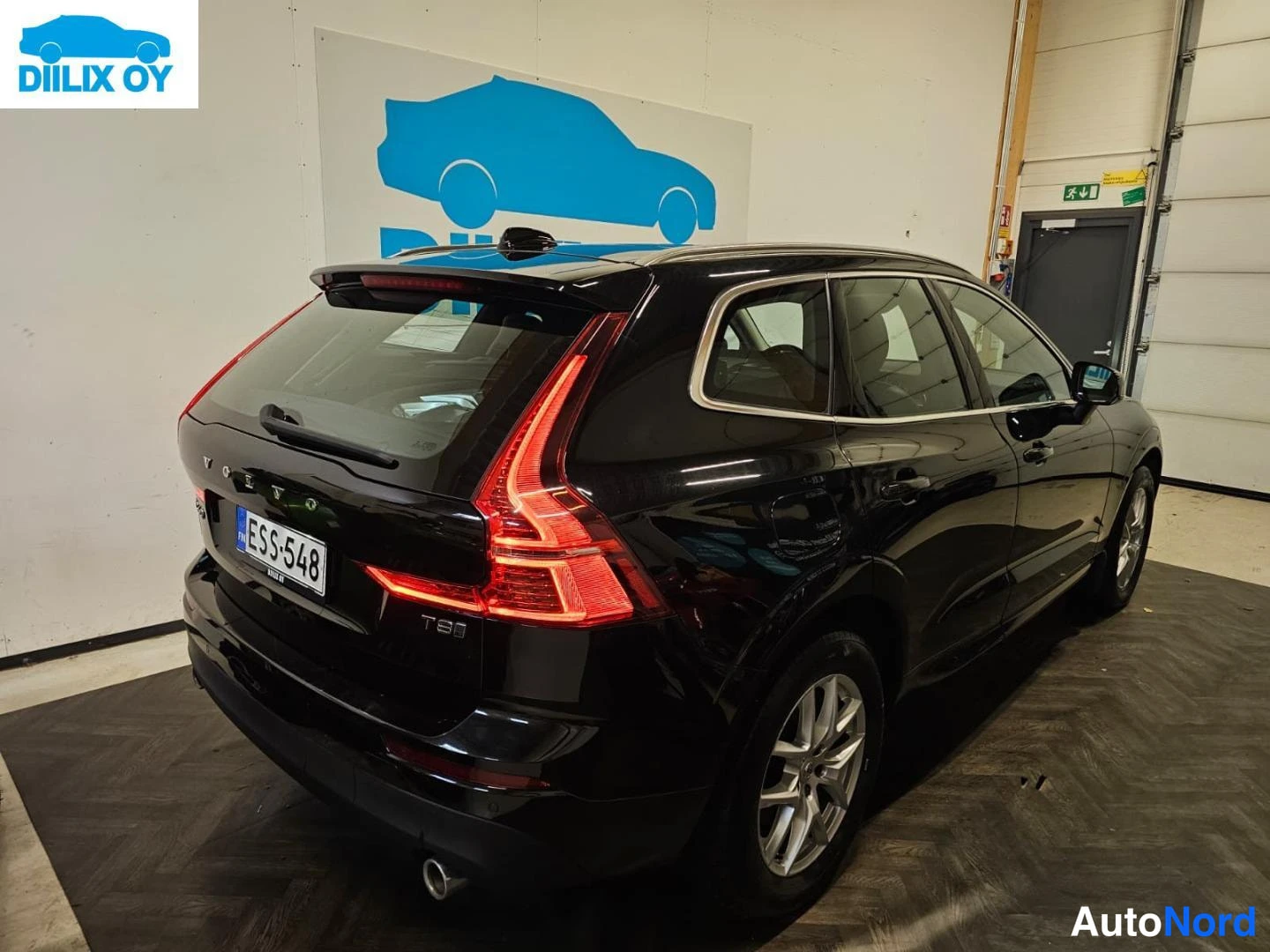 Takaviisto: Mustan Volvo XC60:n takaosa ja vasen kylki sisätiloissa, takavalot punaisina, rekisterikilpi.