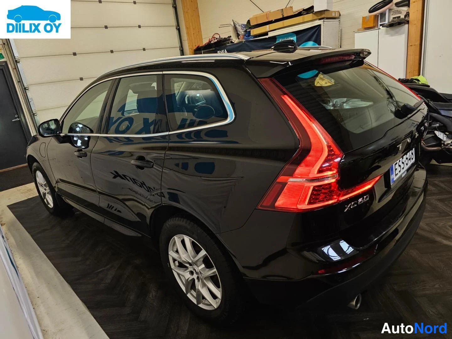 Takaviisto: Mustan Volvo XC60:n takaosa ja vasen kylki tallissa, takavalot punaisina, rekisterikilpi.