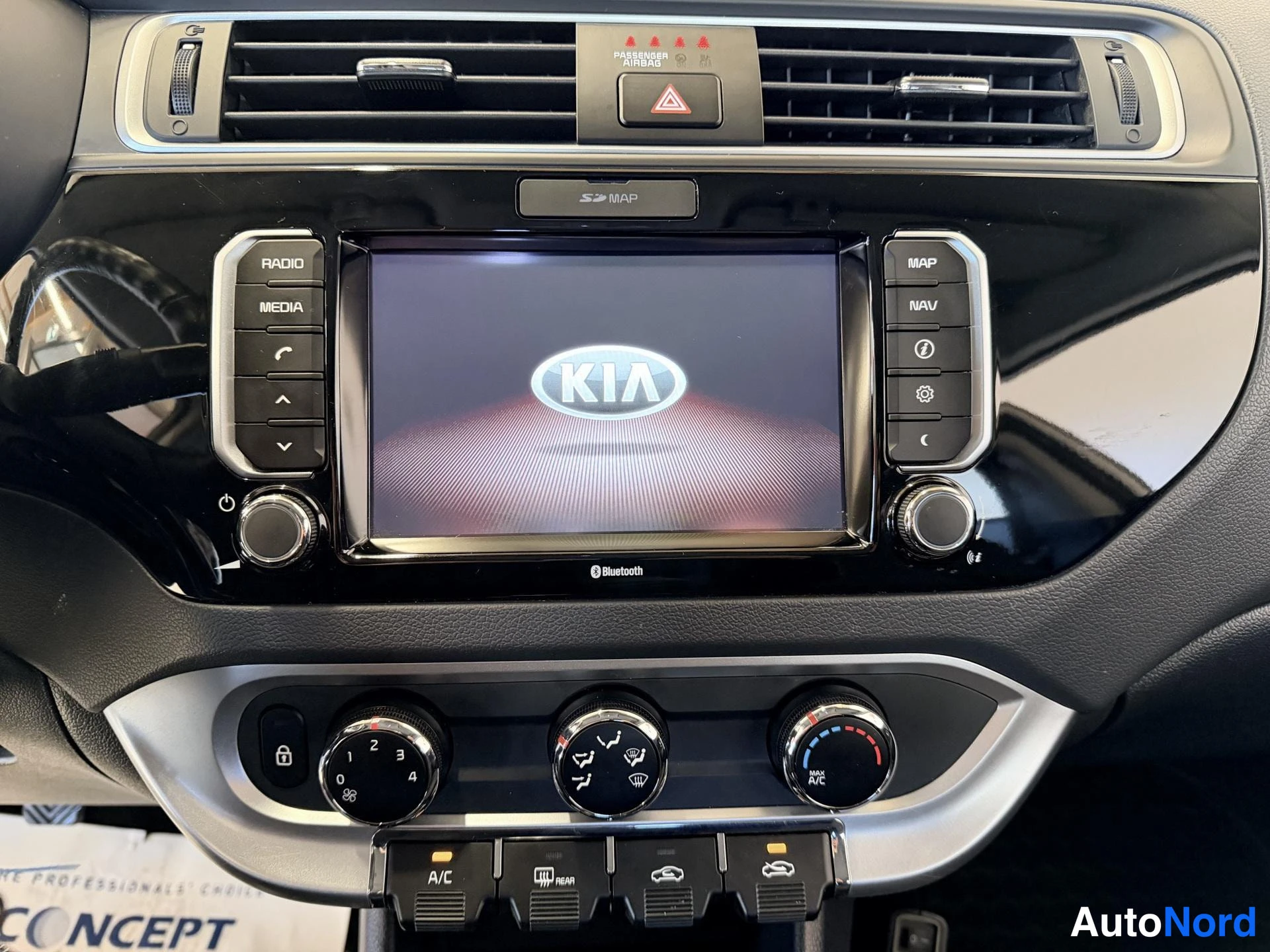 Muu: Kia-merkkisen radion ja ilmastoinnin säädöt lähikuvassa; näytössä KIA-logo ja napit kuten RADIO, MEDIA, MAP, NAV, A/C ja MAX A/C.