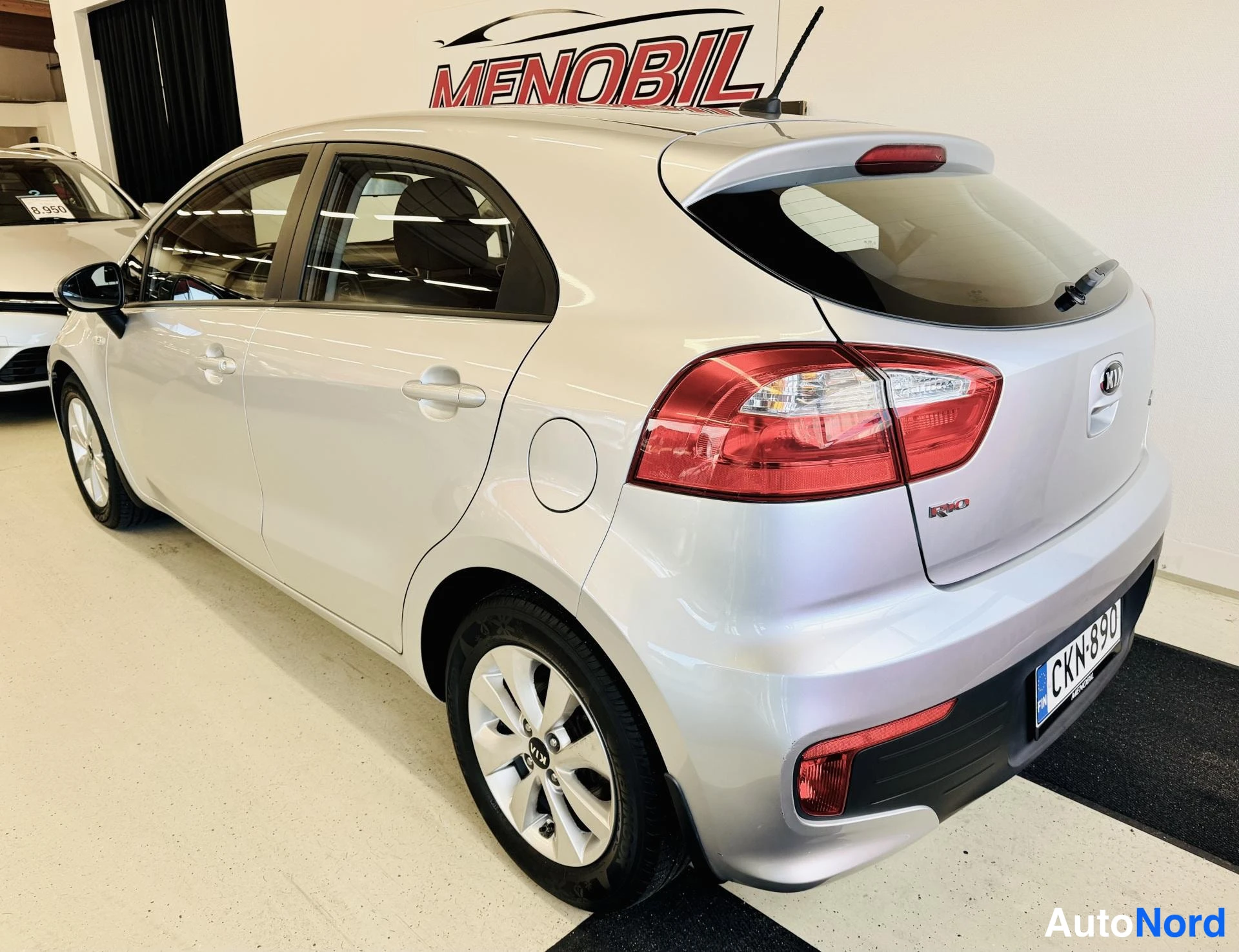 Takaviisto: Kia Rio -henkilöauto vaalean hopeisena takaa vasemmalta kuvattuna, takavalot ja -rekisterikilpi näkyvät.