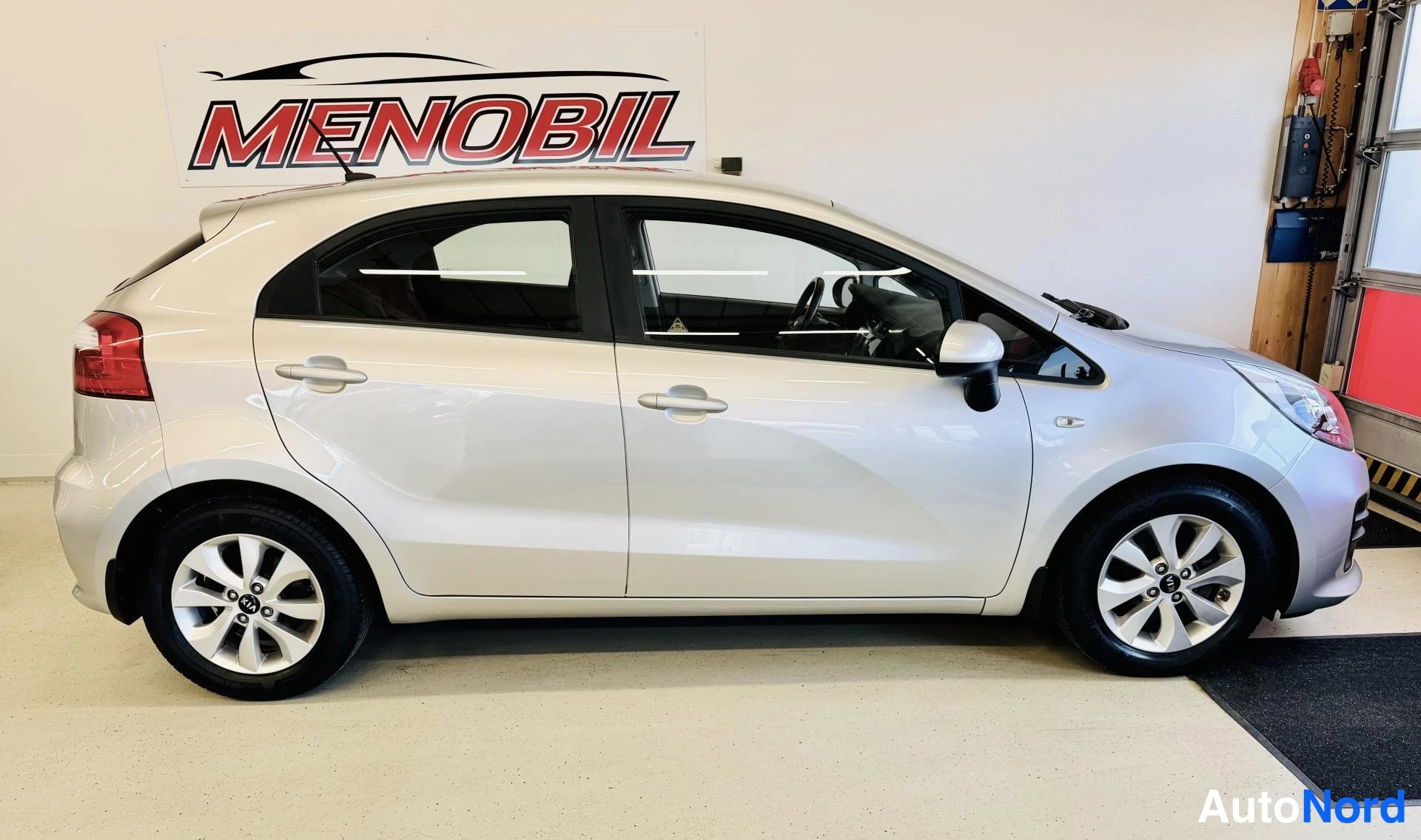 Etuviisto, nokka oikealle: Kia Rio sivulta kuvattuna, hopeanvärinen viistokorinen auto sisätiloissa