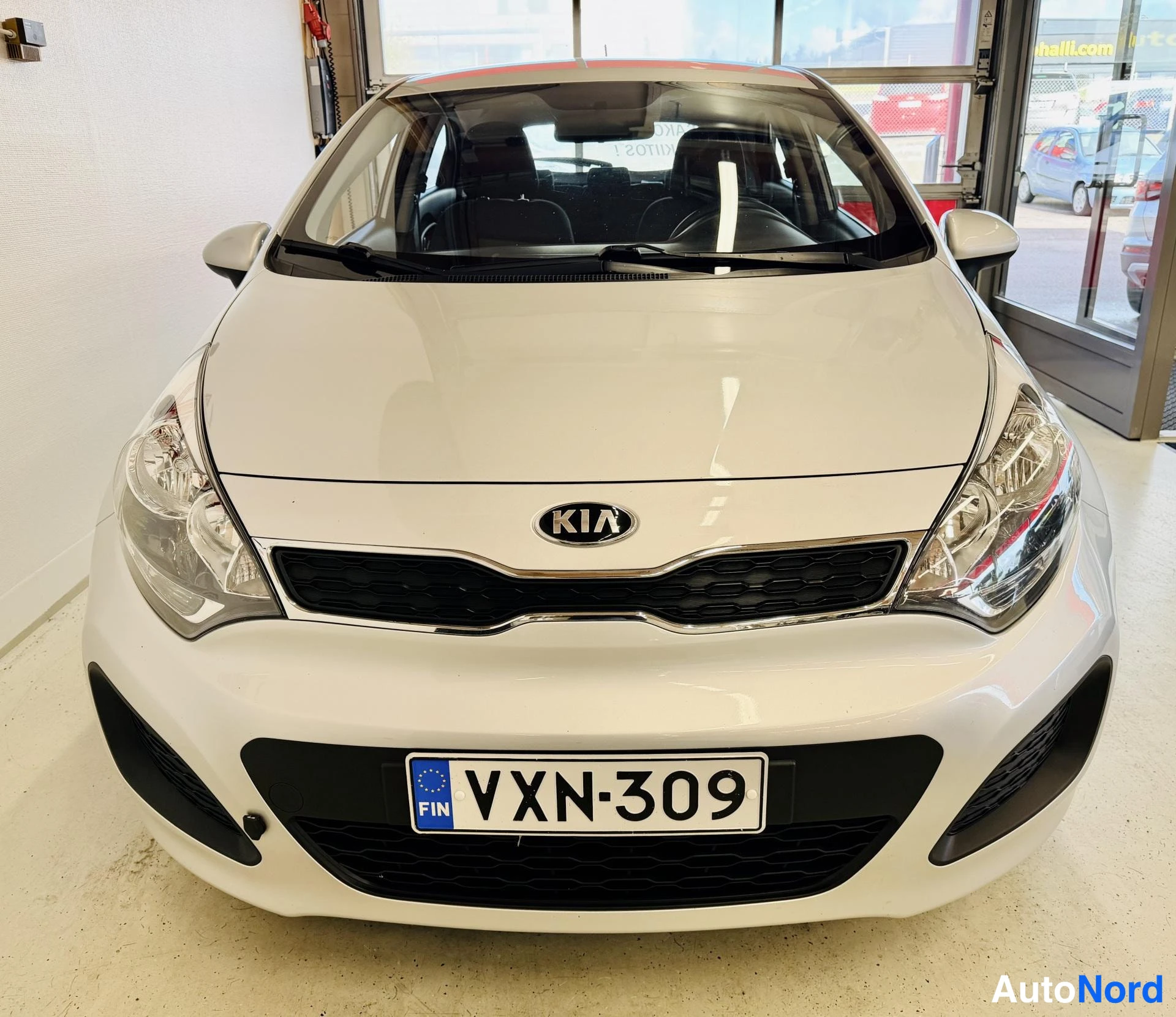 Edestä: Kia Rio:n etupää suoraan edestä: Kia-merkki, KIA-logo etusäleikössä ja rekisteri