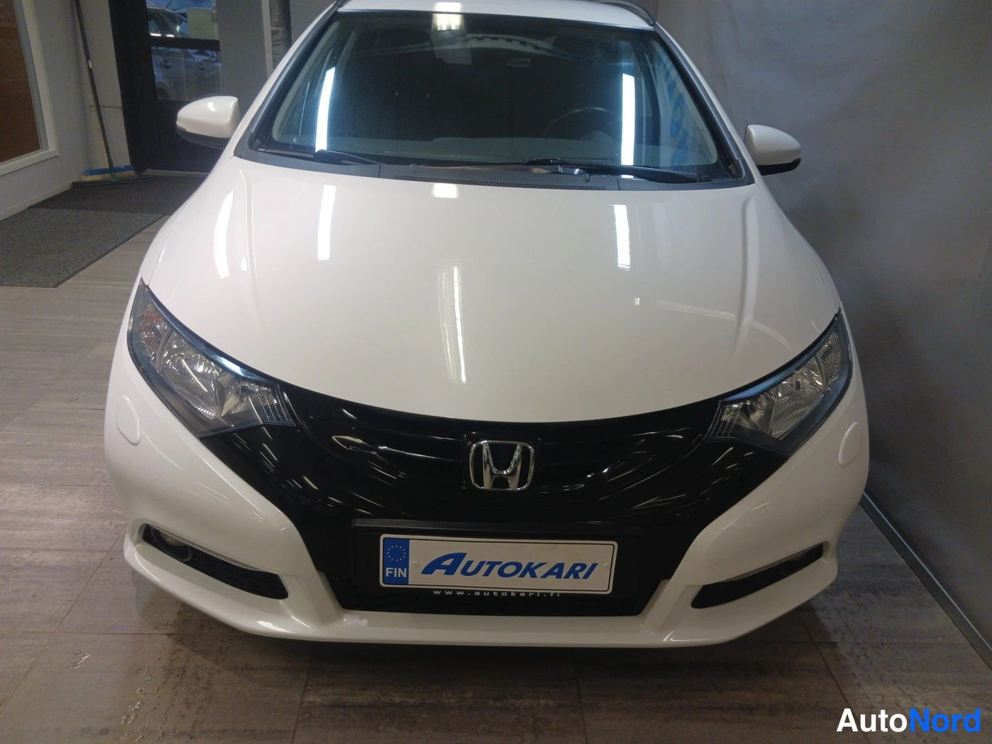 Edestä: Valkoisen Honda Civicin keula suoraan edestä, musta etusäleikkö ja Autokari-tunnus.