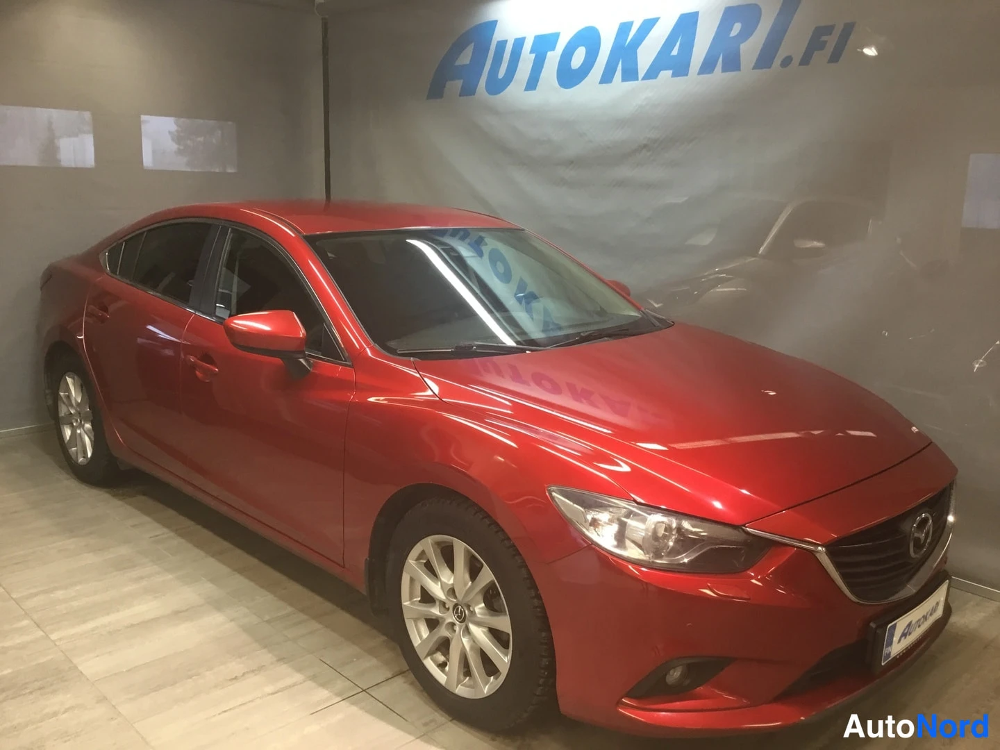 Etuviisto, nokka oikealle: Punainen sedan henkilöauto etukulmasta oikealle suunnattuna valokeitaan myyntitilassa.