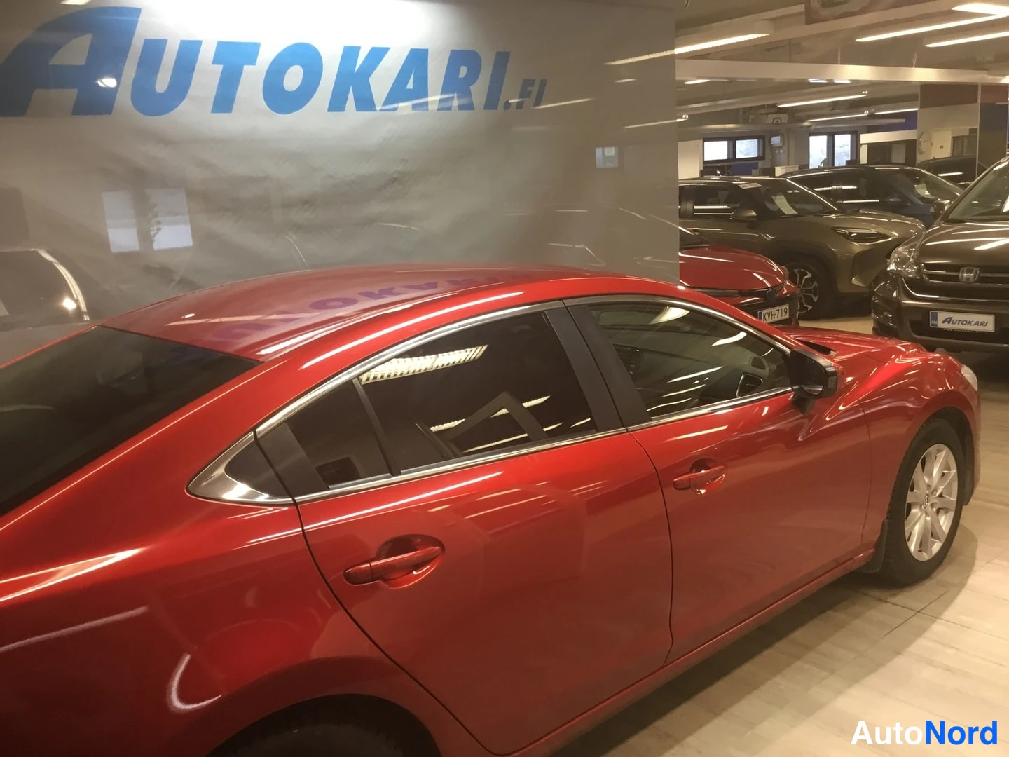 Sivulta: Punaisen auton vasen kylki sivukulmasta näkyvissä autonäyttelytilassa.