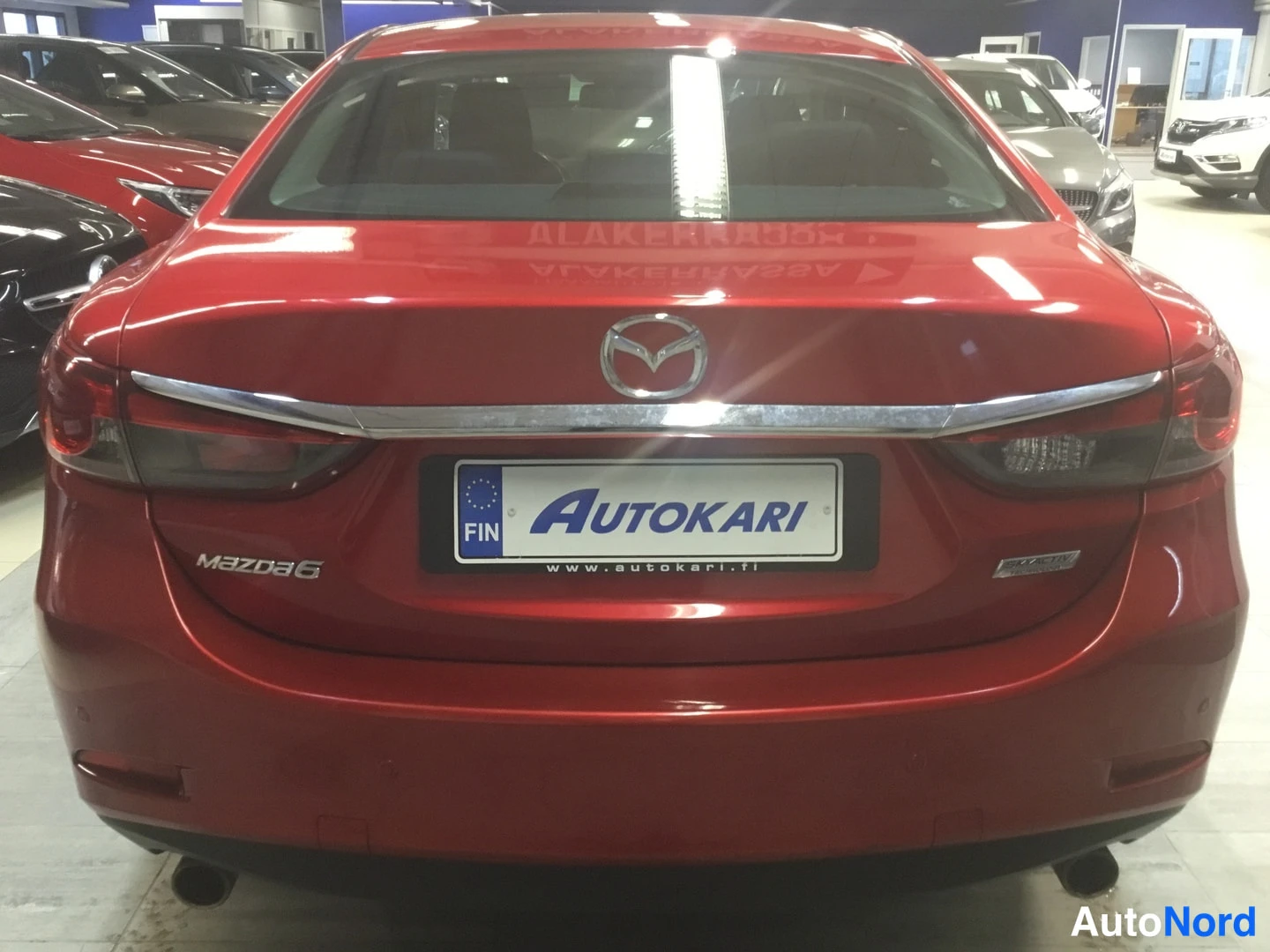 Takaa: Punaisen Mazda 6:n takapää suoraan takaa kuvattuna; näkyvissä takavaloissa, Mazda-merkki, Mazda6-teksti ja Autokari-kilpi.