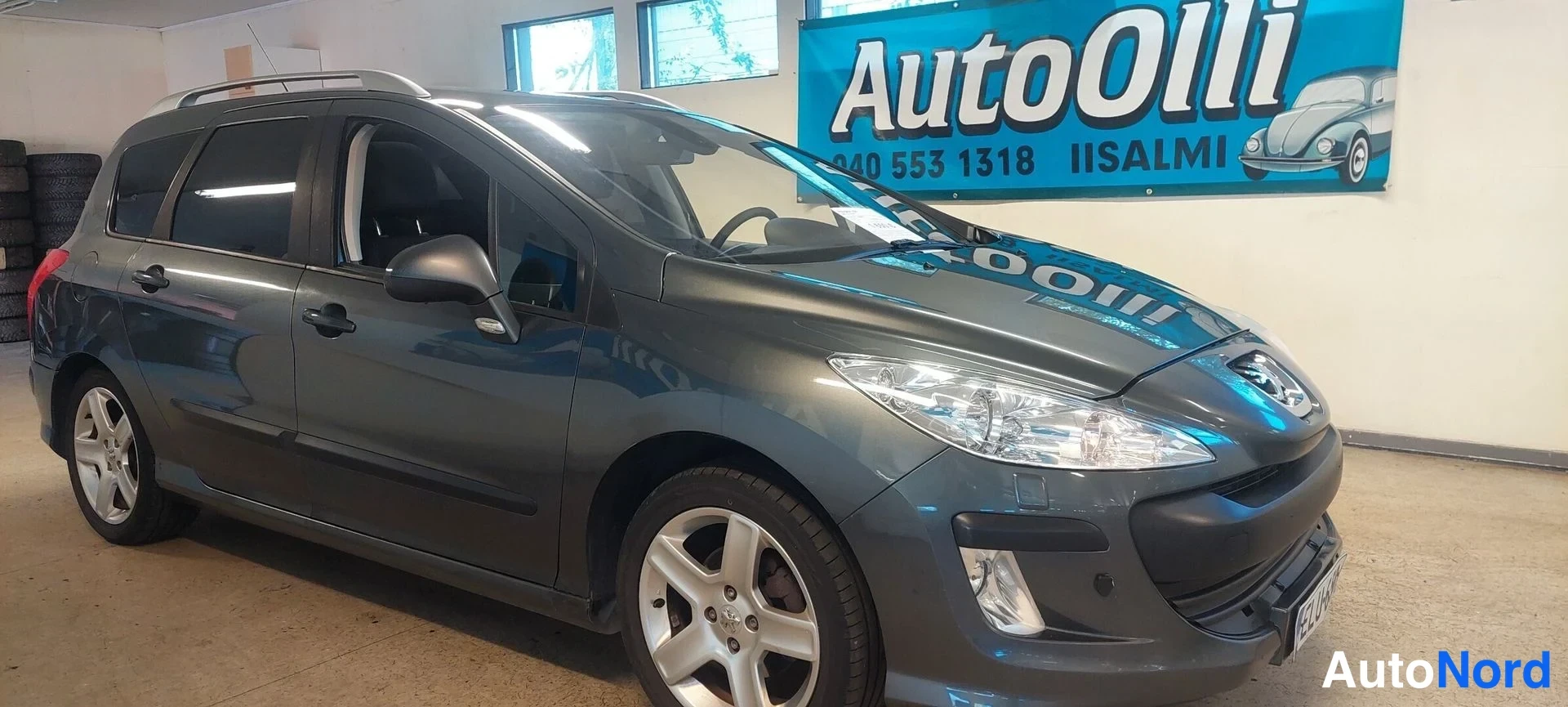 Etuviisto, nokka oikealle: Peugeot 308 SW farmari näkyy etuosasta ja oikealta sivulta liiketilan sisällä, tummanharmaa