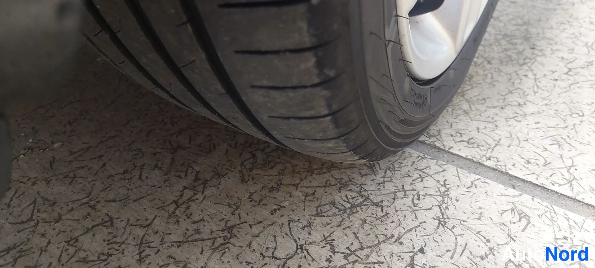 Yksityiskohta: Kulunut autotiskia rengas kiveen asennettuna, näkyy parta juova ja rei'itys.