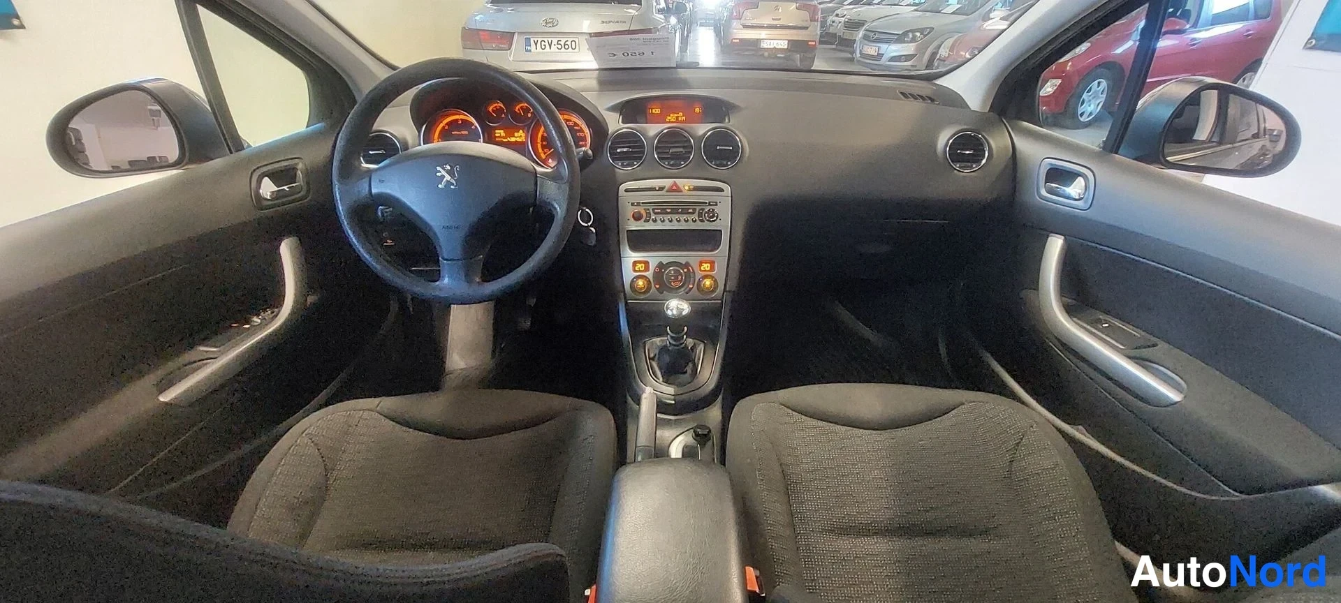 Etuviisto, nokka vasemmalle: Auto sisäpuolelta, kojeisto ja mittarit näkyvät peugeot-merkkinä, mustat kangaspenkit ja manuaalivaihtoeja.