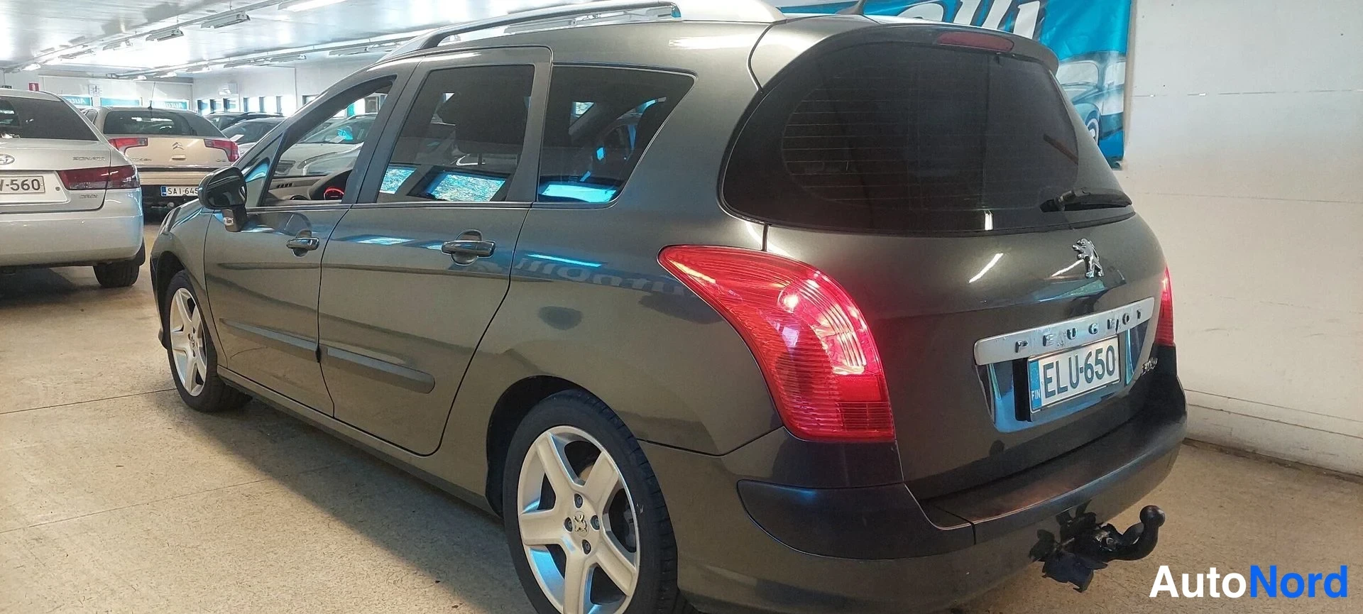 Takaviisto: Peugeot 308 SW farmari näkyy perästä ja vasemmalta sivulta autotallissa, rekisterikilpi, vetokoukku, katolla kromilista