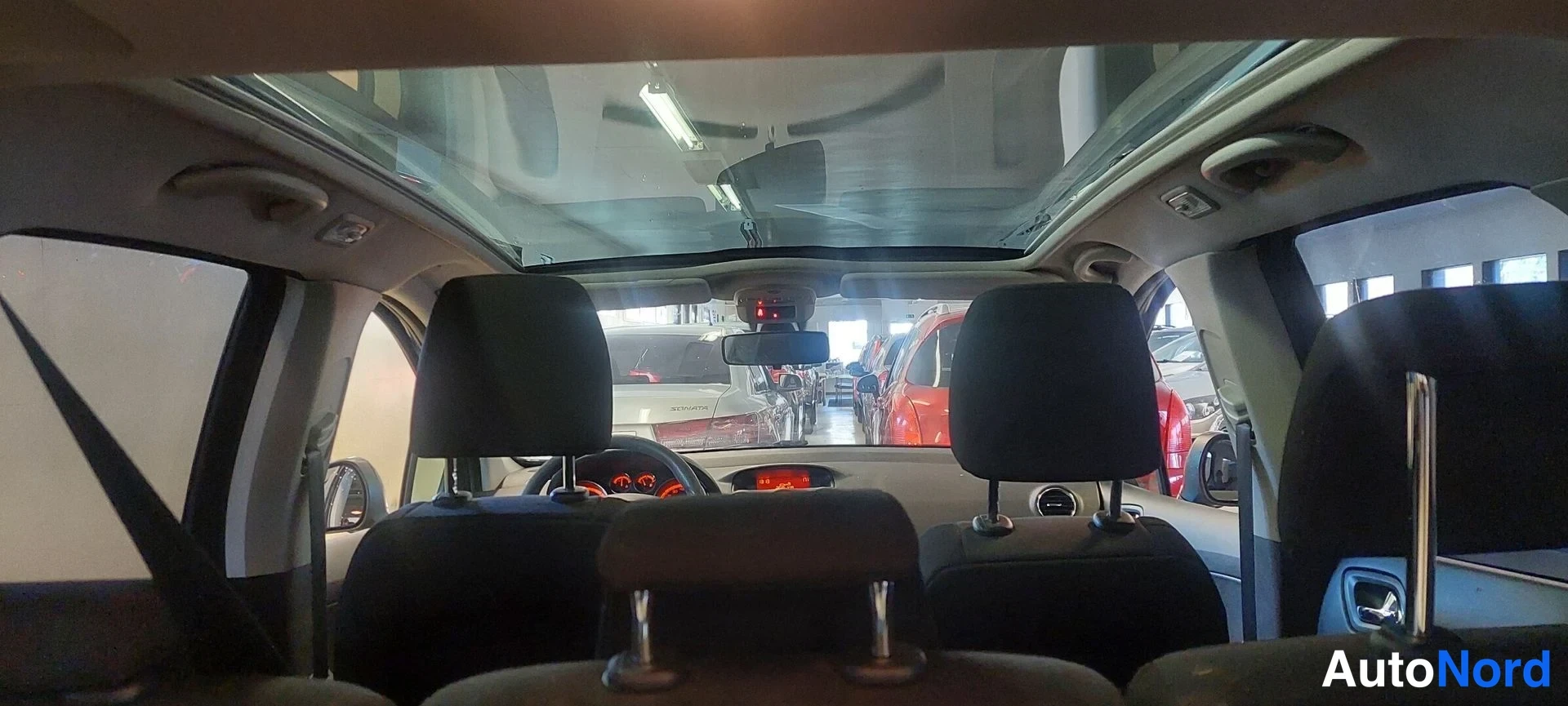 Yksityiskohta: Näkymä auton takaistuimelta eteenpäin: panssarilasi, tuulilasin takana seisovat autot ja ohjaamon sisävalaisin.