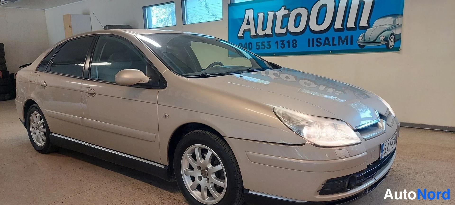 Etuviisto, nokka oikealle: Kultaiseen sävyyn maalattu Citroen C5 -sedan kulissit kuvattuna etuosa oikealta eteenpäin sisätiloissa.