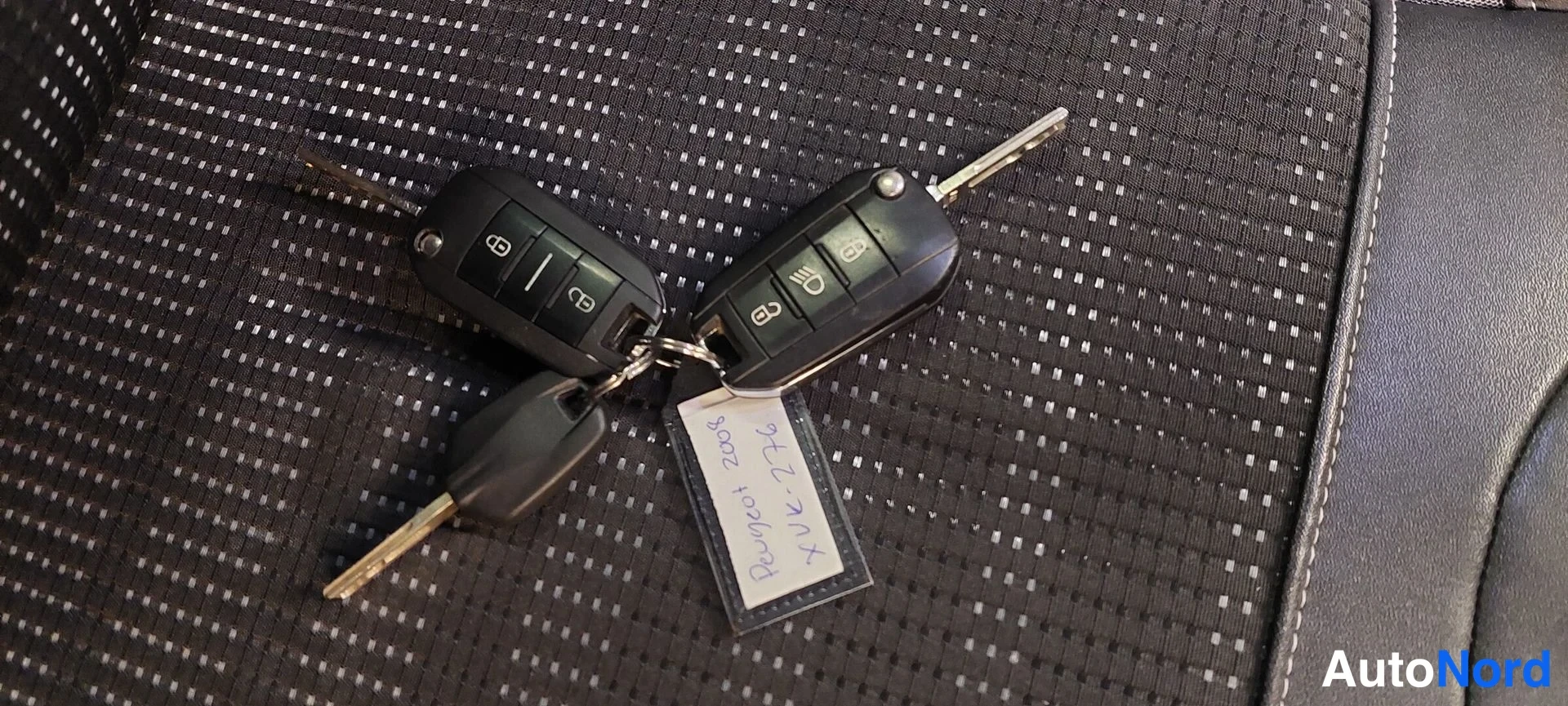 Yksityiskohta: Kaksi avaimenperää tummalla tekstiilipenkillä; lappu jossa käsin kirjoitettu Peugeot 2008 ja rekisteritunnus.