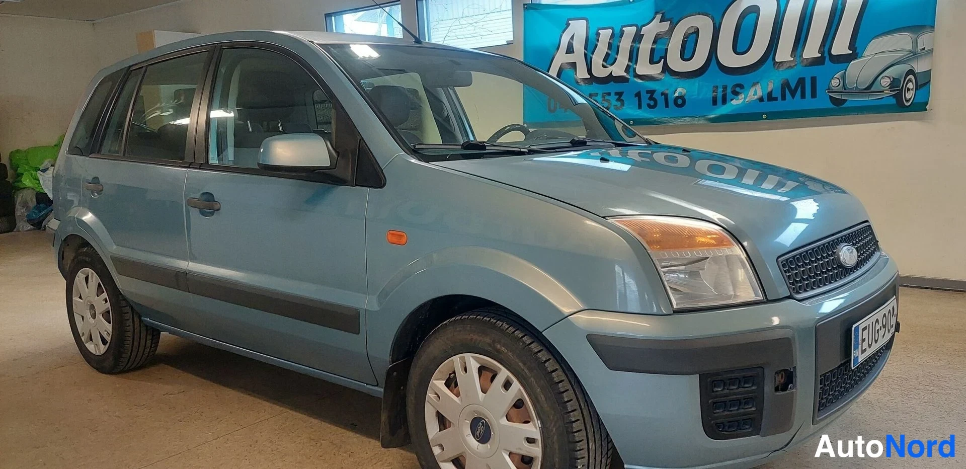 Etuviisto, nokka oikealle: Ford Fusion -farmariauto etuviistestä oikealta, vaaleansininen korivalmiissa tilassa sisätiloissa, rekisterikilpi.