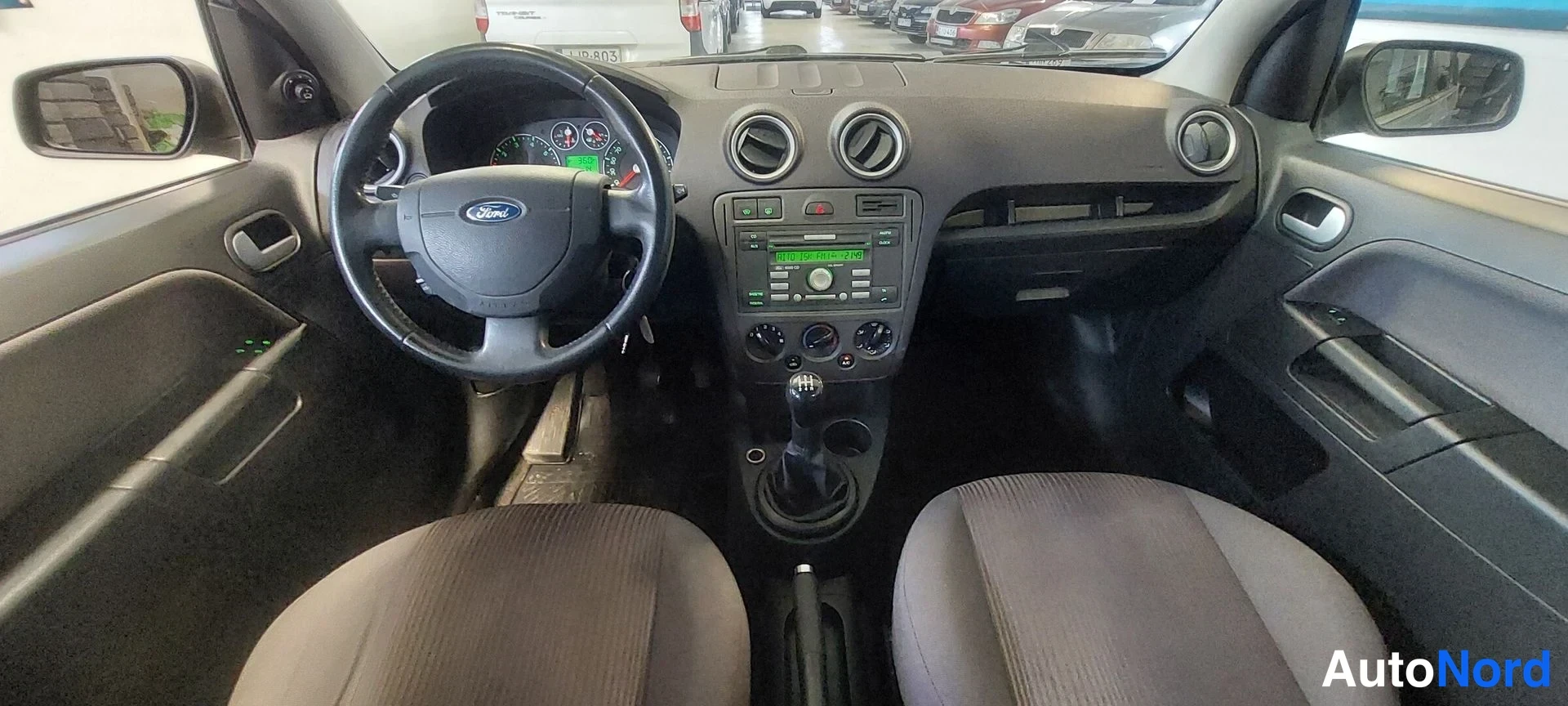 Sivulta: Ford-instrumentit: ohjauspyörä, manuaalivaihteisto, radio-näyttö keskikäyttötaulussa ja kaksi etuistuinta.